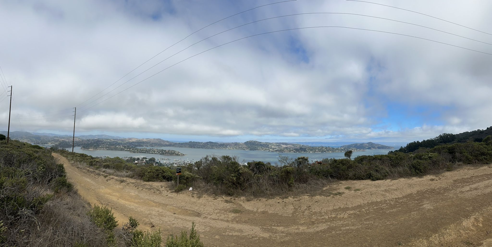 Panoramic view of a bay with hills and cloudy sky from a dirt road. - Battery Townsley – Horse Barn loop from Marin City