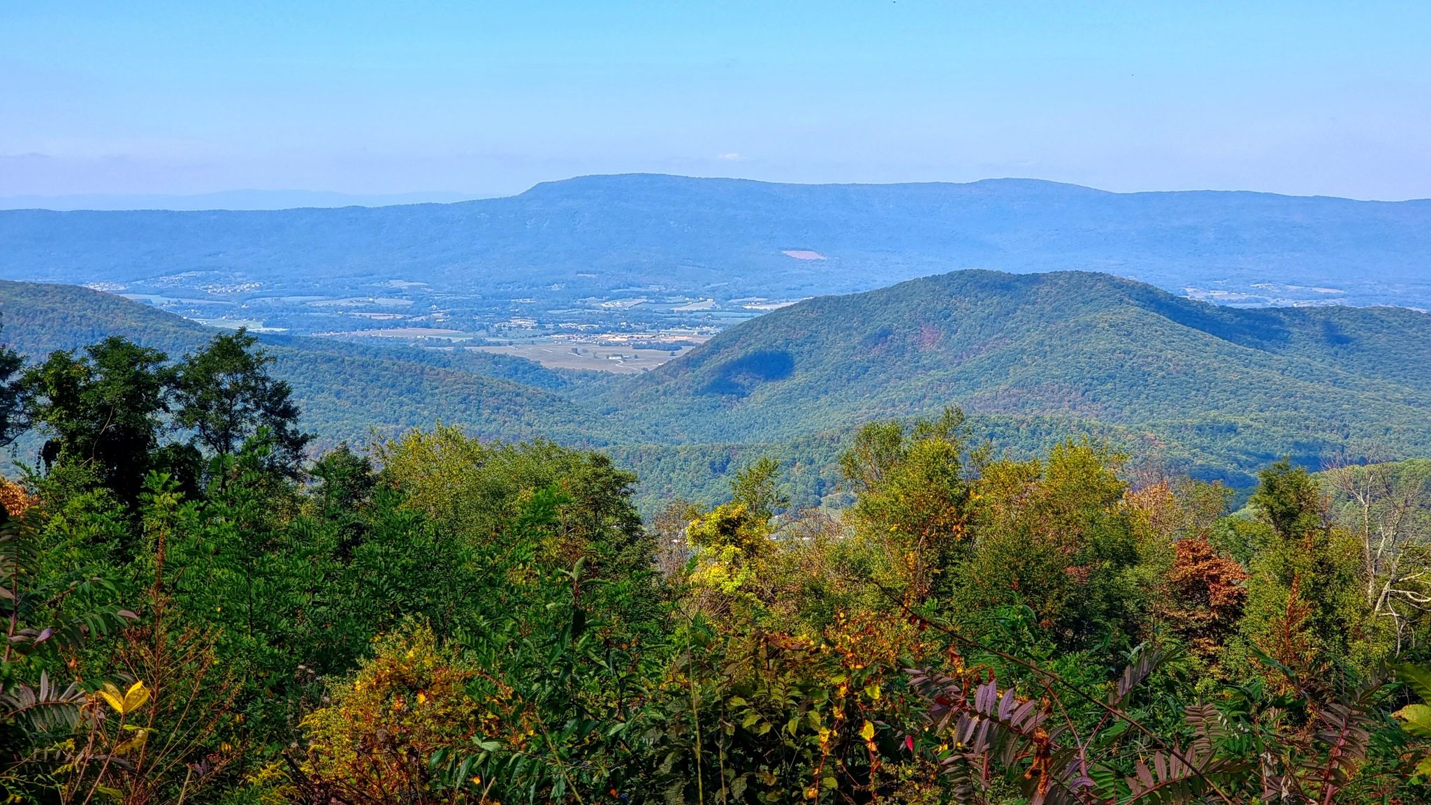 Distant mountains and valley seen through green and autumn-colored trees. - View from Hightop – Swift Run Overlook loop from Smith Roach Gap