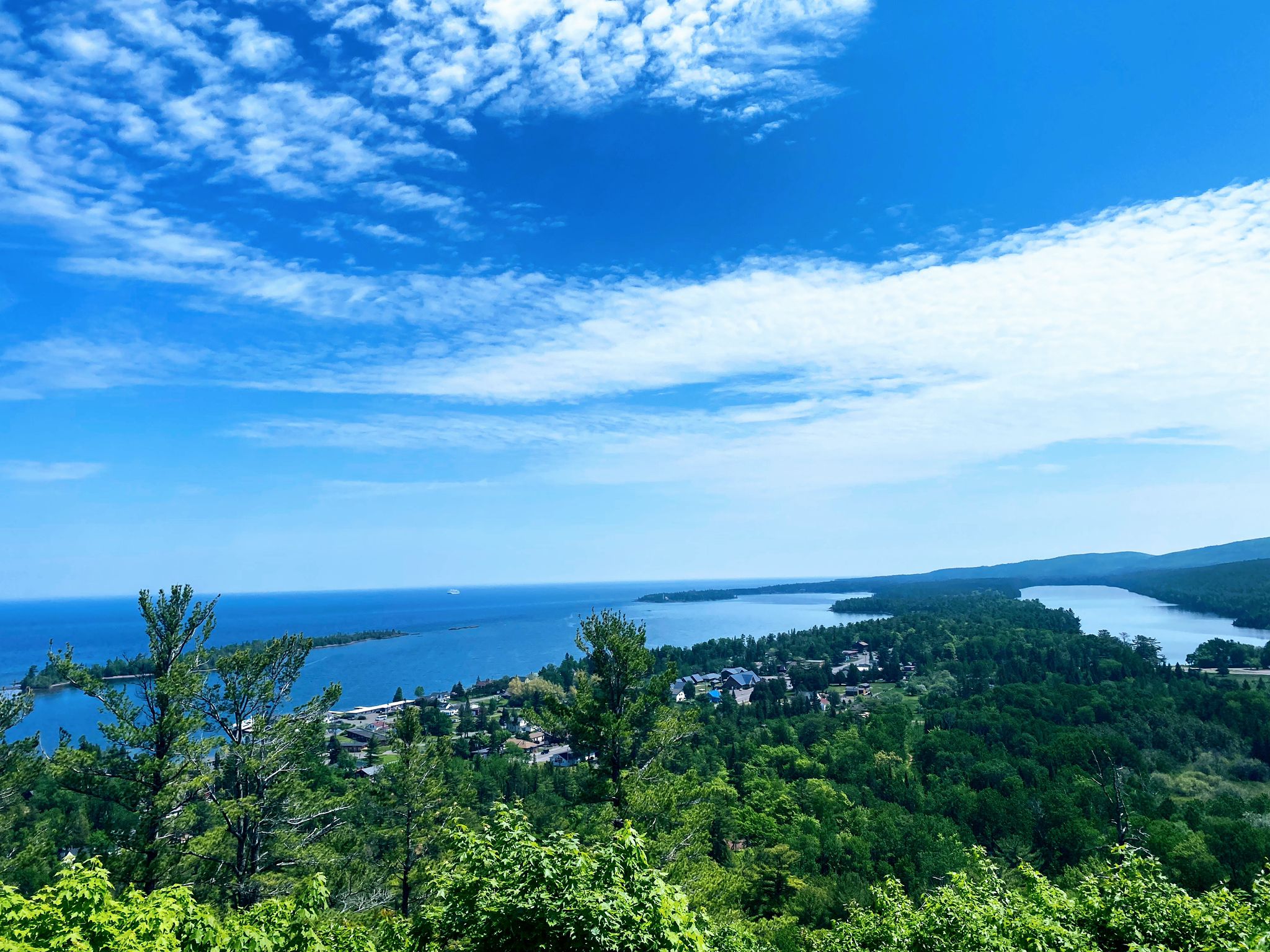 Vast blue lake and green forests under a bright, cloudy sky. - Brockway Nose – Epic woodwork - fun trail feature loop from Copper Harbor