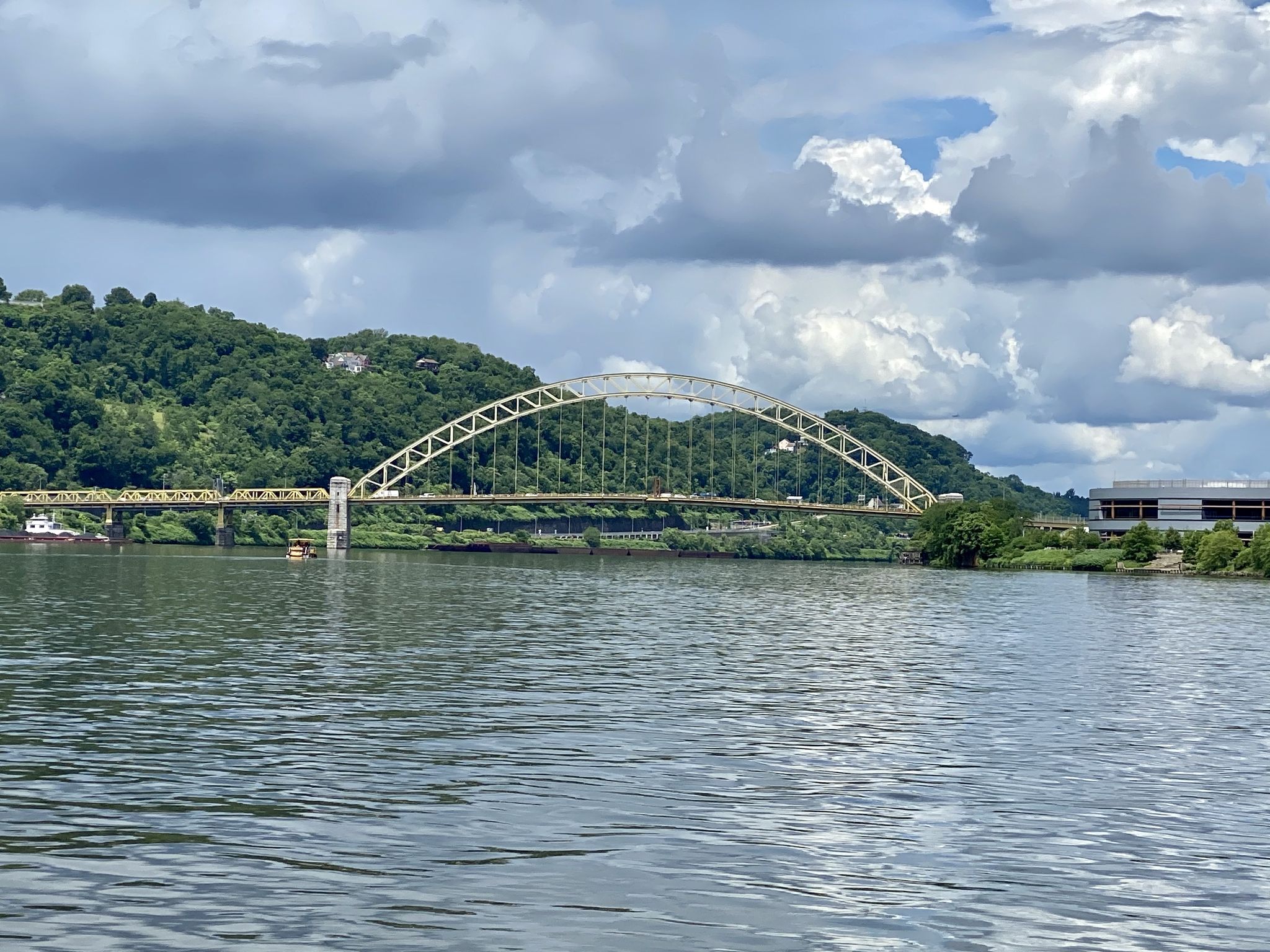 Large yellow arched bridge over a wide river under cloudy skies. - Three Rivers Heritage Trail Loop
