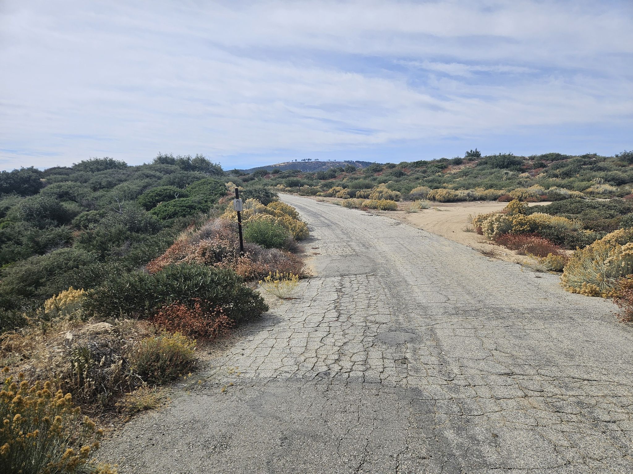 Cracked asphalt road winding through dry, brushy hills under a cloudy sky. - Mount Gleason Loop