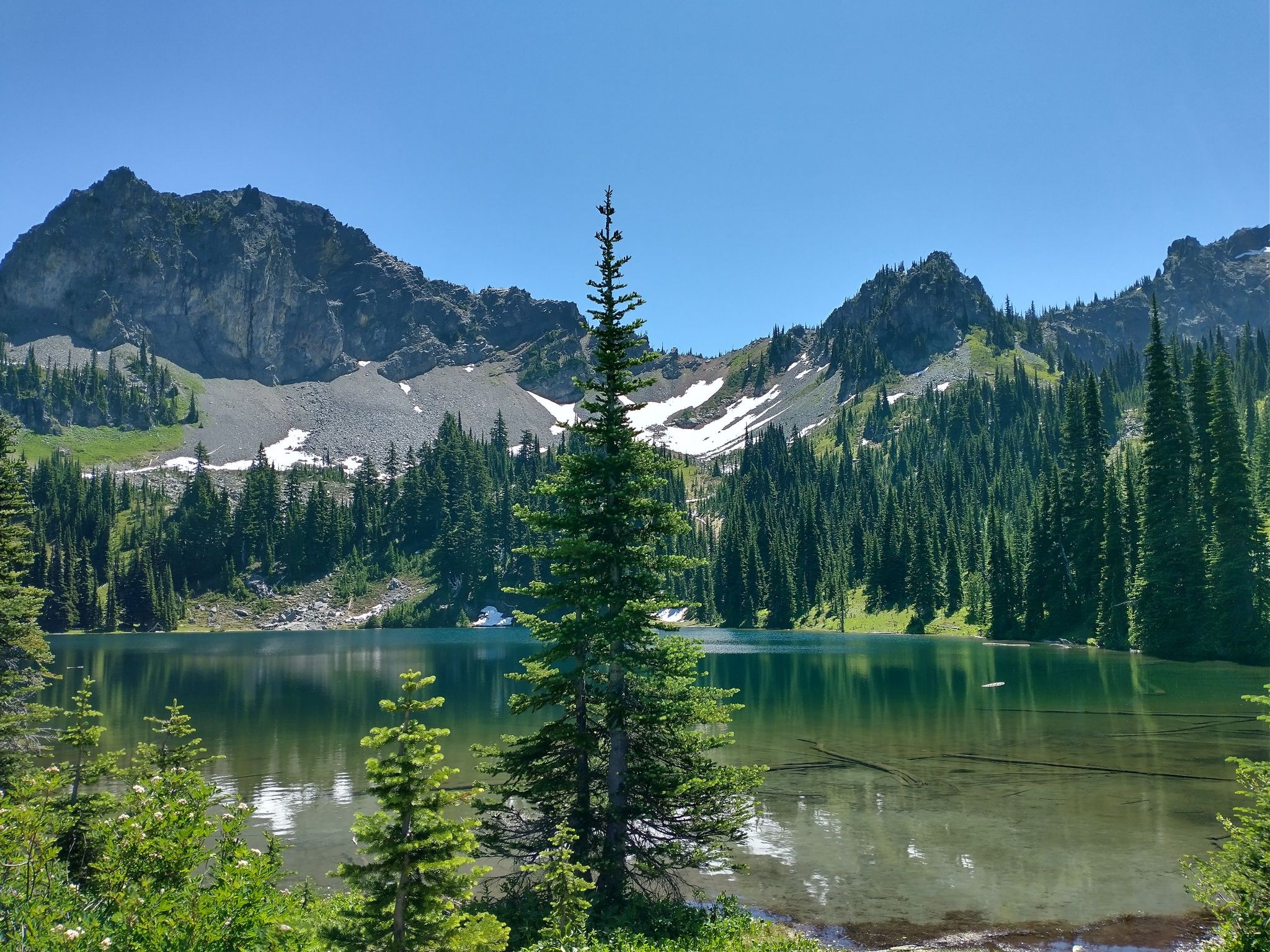 Sunny mountain lake with pine trees and rocky peaks, some snow visible. - Crystal Lake via Sourdough Gap and Sheep Lake