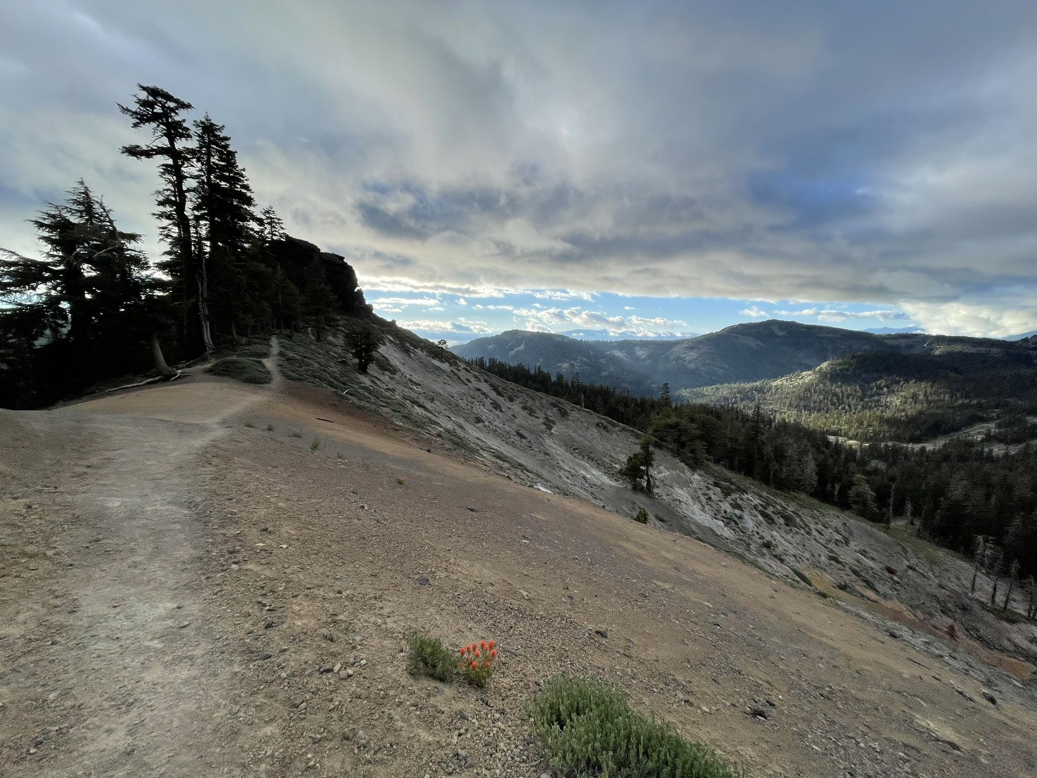 A dirt path on a steep, barren hillside under a dramatic cloudy sky. - Tahoe Rim Trail: Barker Pass to Tahoe City