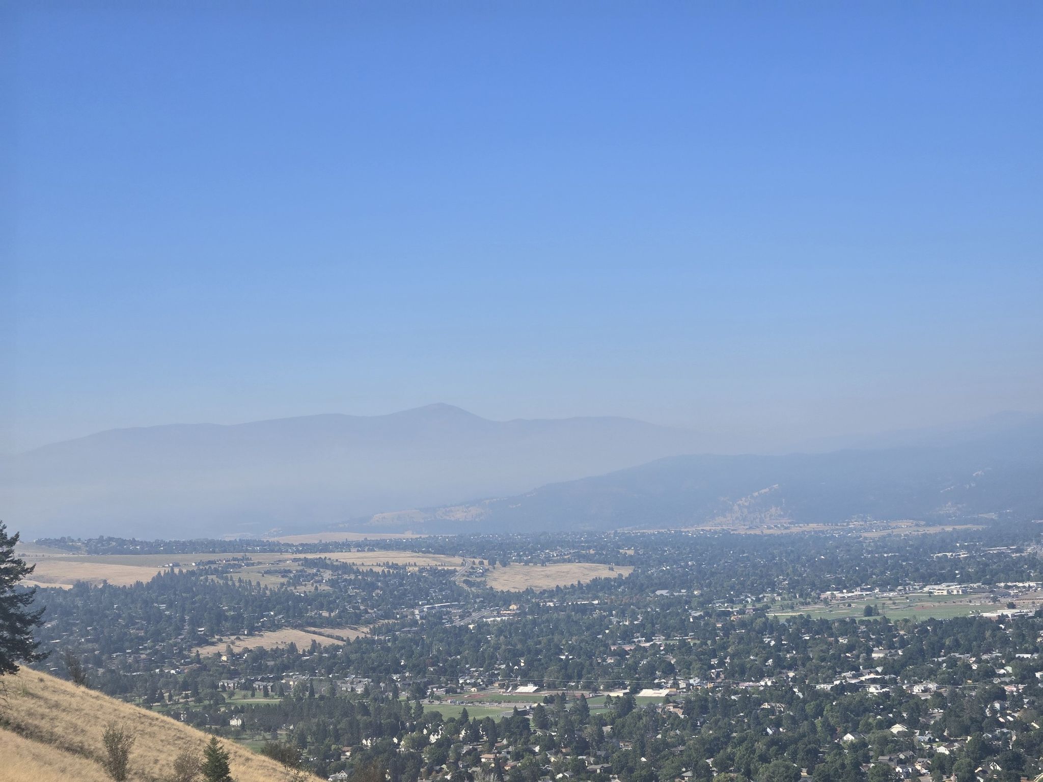 Expansive view of a town nestled in a valley with hazy distant mountains. - The M Trail on Mount Sentinel – Mount Sentinel loop from Missoula