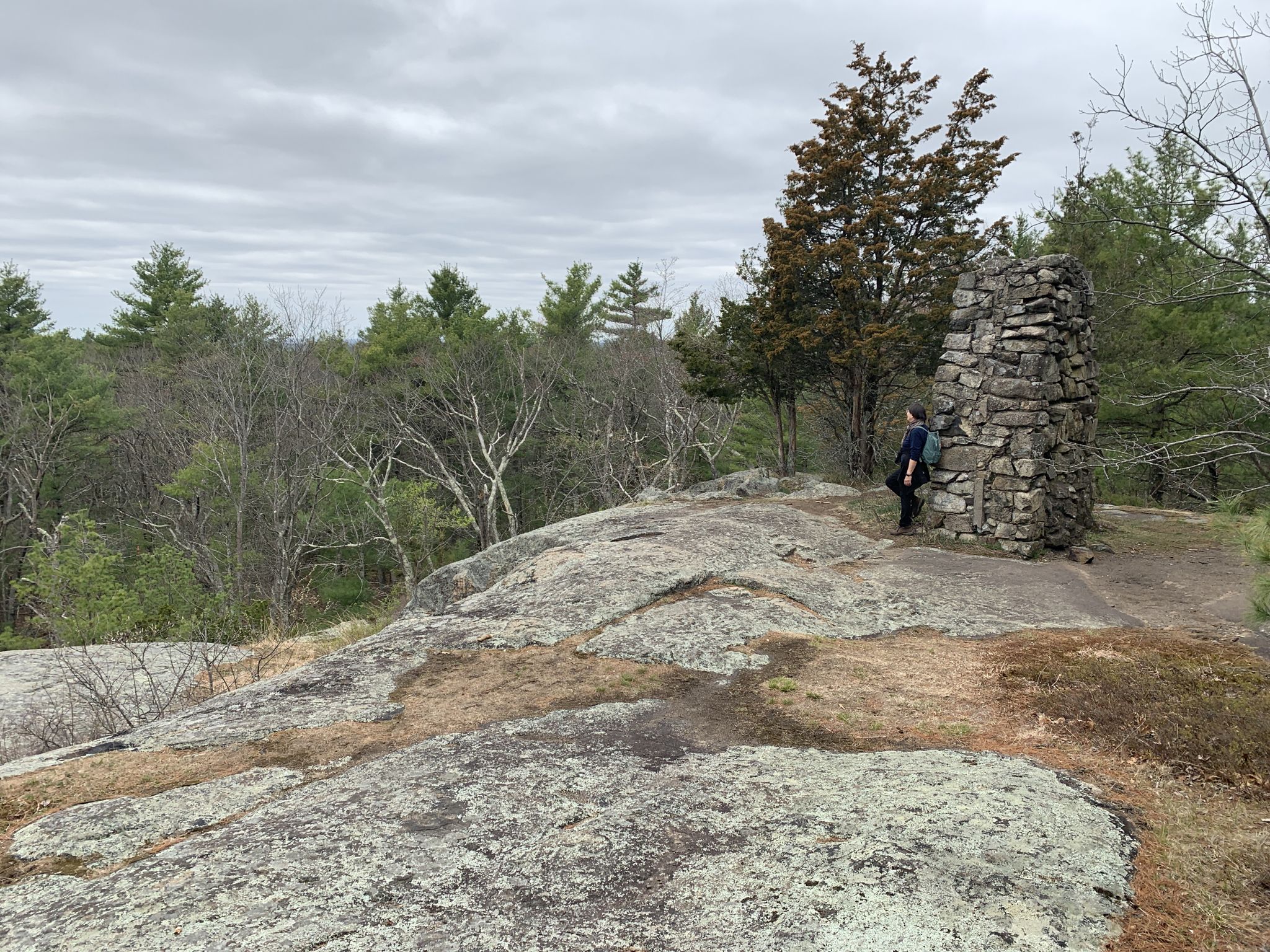 Person stands by a stone cairn on a rocky hill under an overcast sky. - Bluff Trail