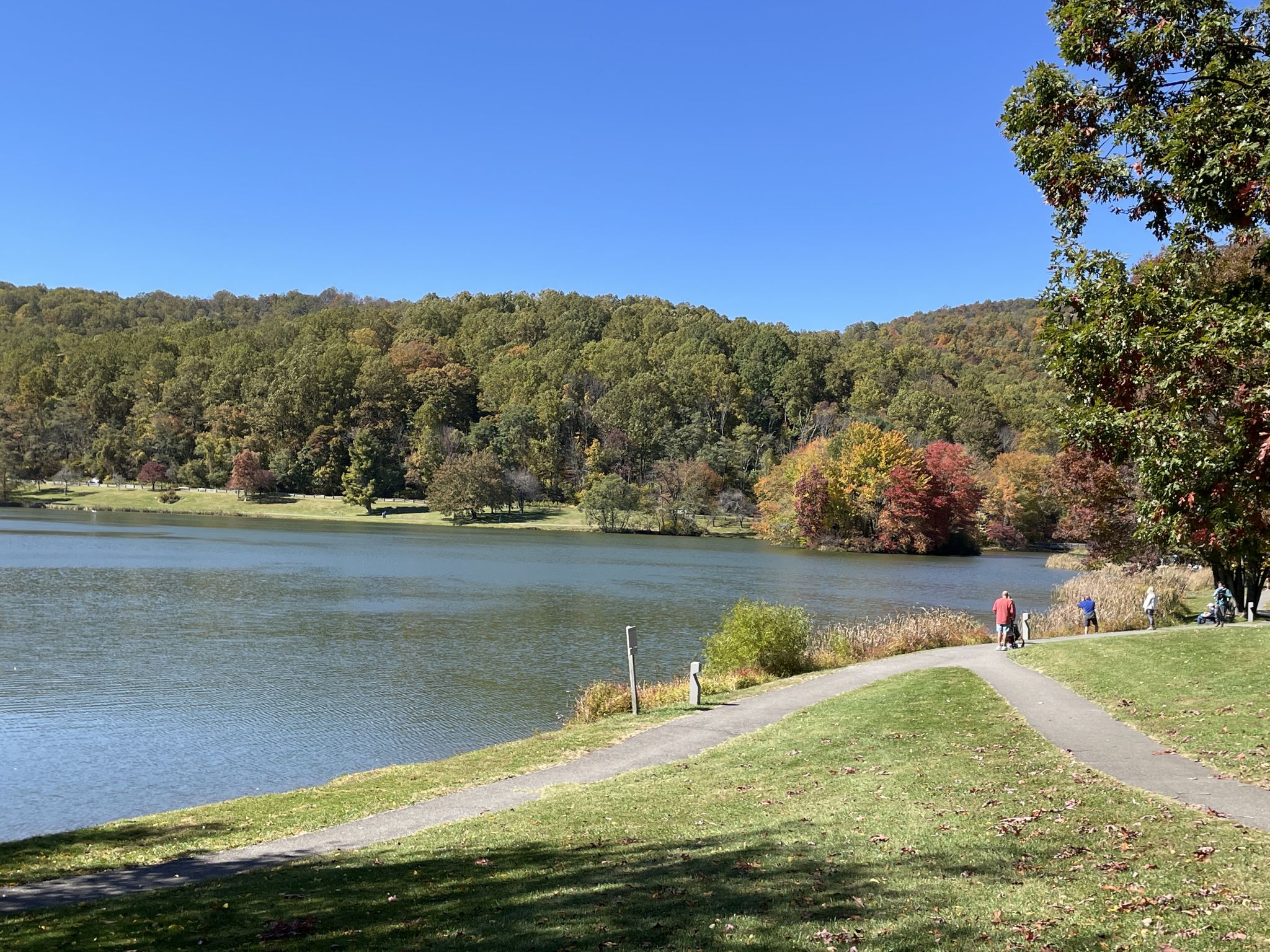 People walk on a path beside a lake with colorful autumn trees under a clear sky. - Flat Top Trail