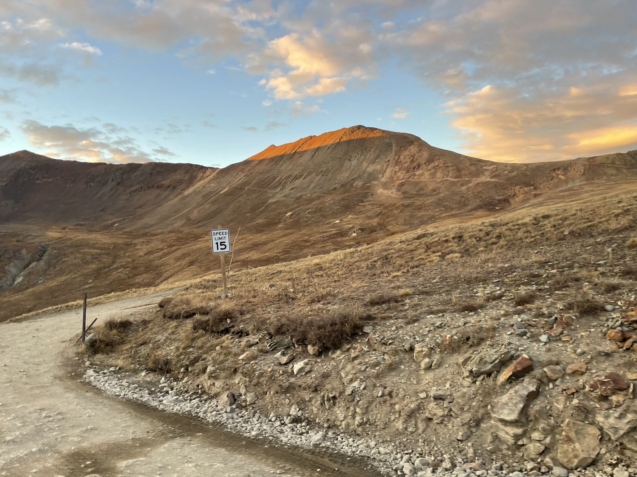 Dirt road winding up a mountain with a speed limit sign at sunset. - Cinnamon Pass Road via Animas Forks