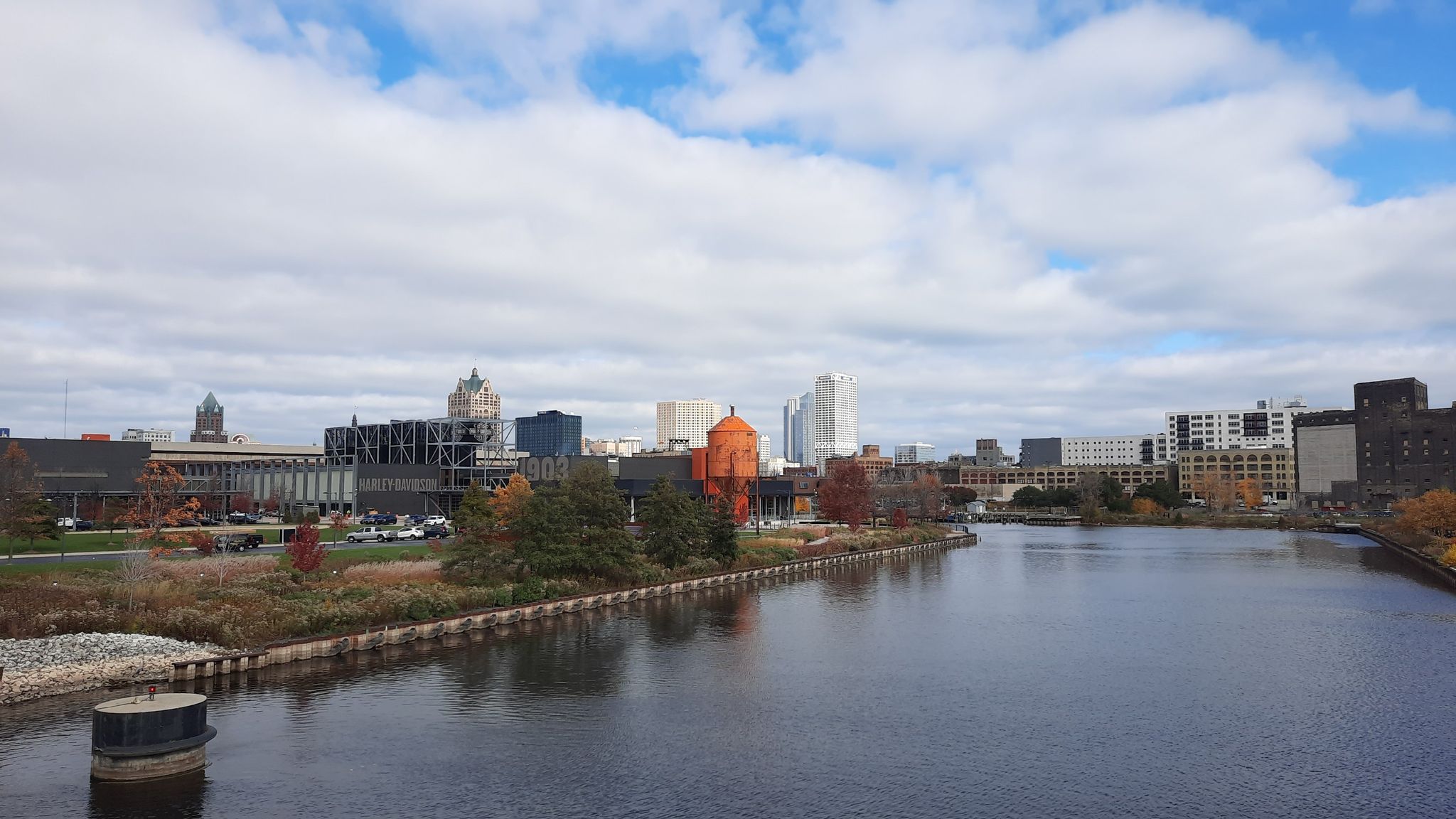 City skyline with a river and autumn trees under a cloudy sky. - Hank Aaron State Trail