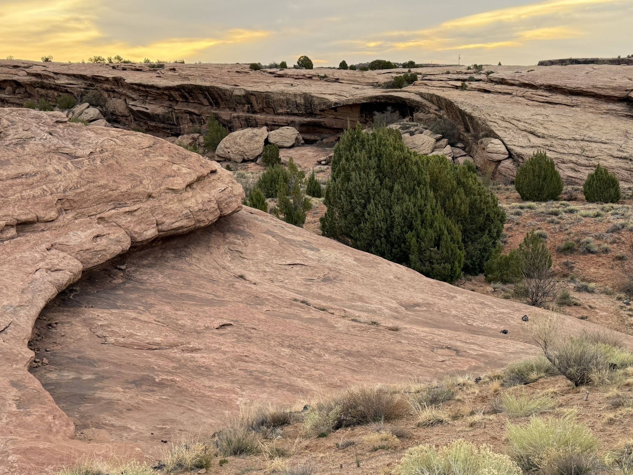 Desert landscape with red rock formations and green bushes under a cloudy sky. - Tseyi Overlook loop from Canyon de Chelly Visitor Center