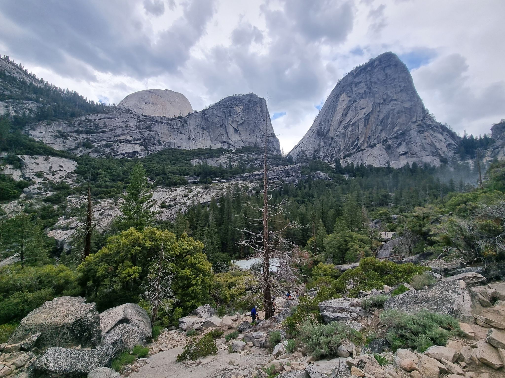Majestic granite mountains and pine forests under a cloudy sky, with a distant hiker. - Vernal Fall and Clark Point Loop via Mist Trail and John Muir Trail
