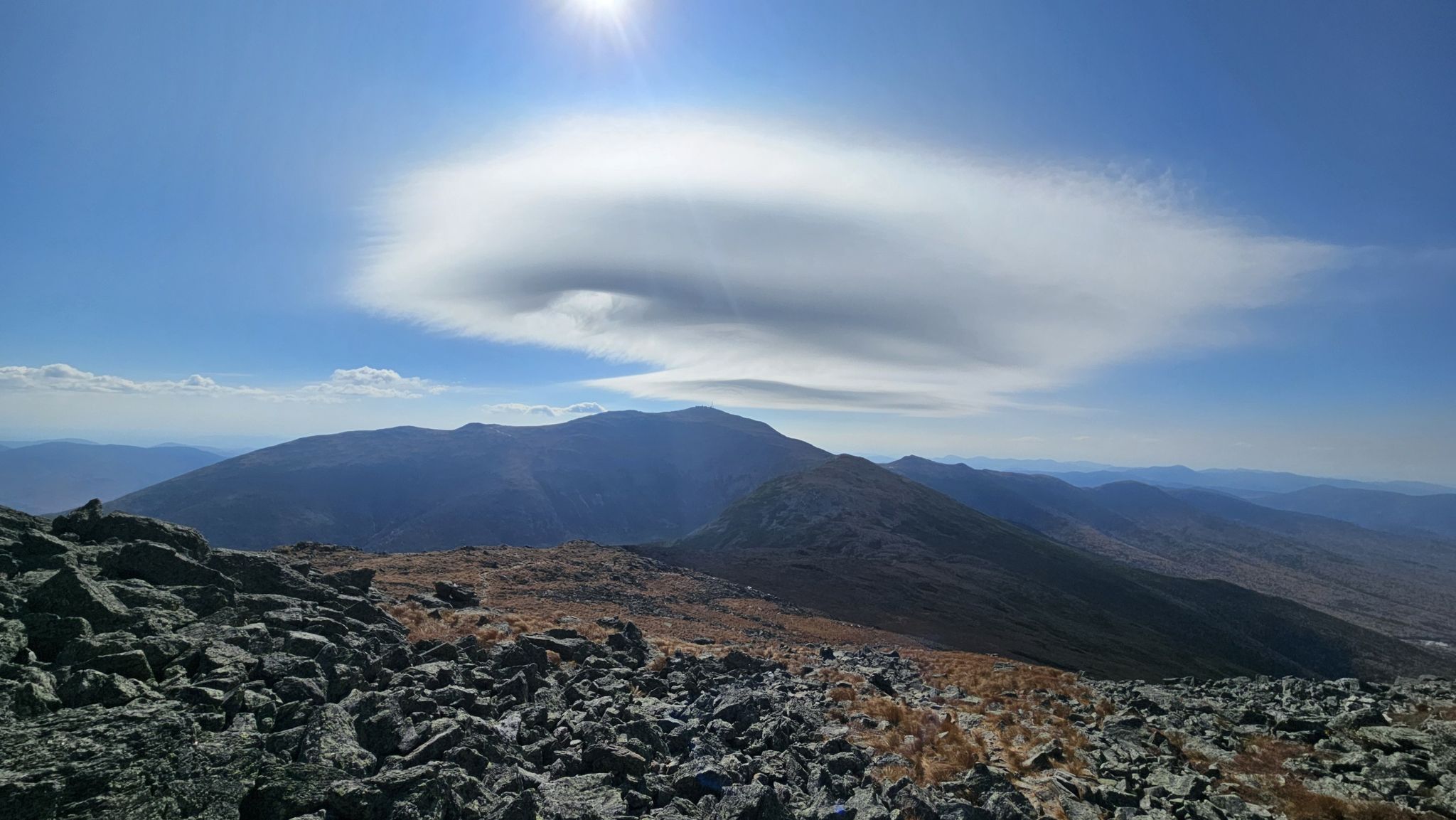 A bright sun shines over a unique cloud above a rocky mountain landscape. - Mount Jefferson Loop via Caps Ridge Trail
