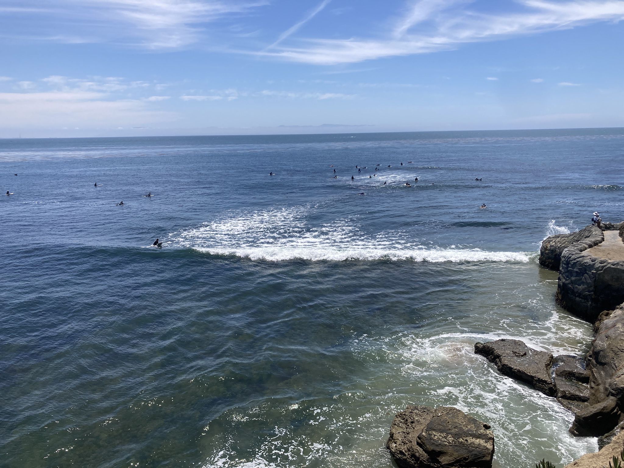 Ocean with many surfers, breaking waves, and rocky cliffs under a bright sky. - Pleasure Point Beach – Moran Lake Beach and Park loop from Capitola
