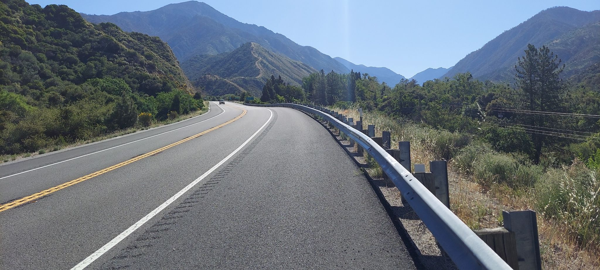 Winding road with a guardrail, leading into a green mountain valley, sunny. - Santa Ana River Trail loop (Post Office Section)