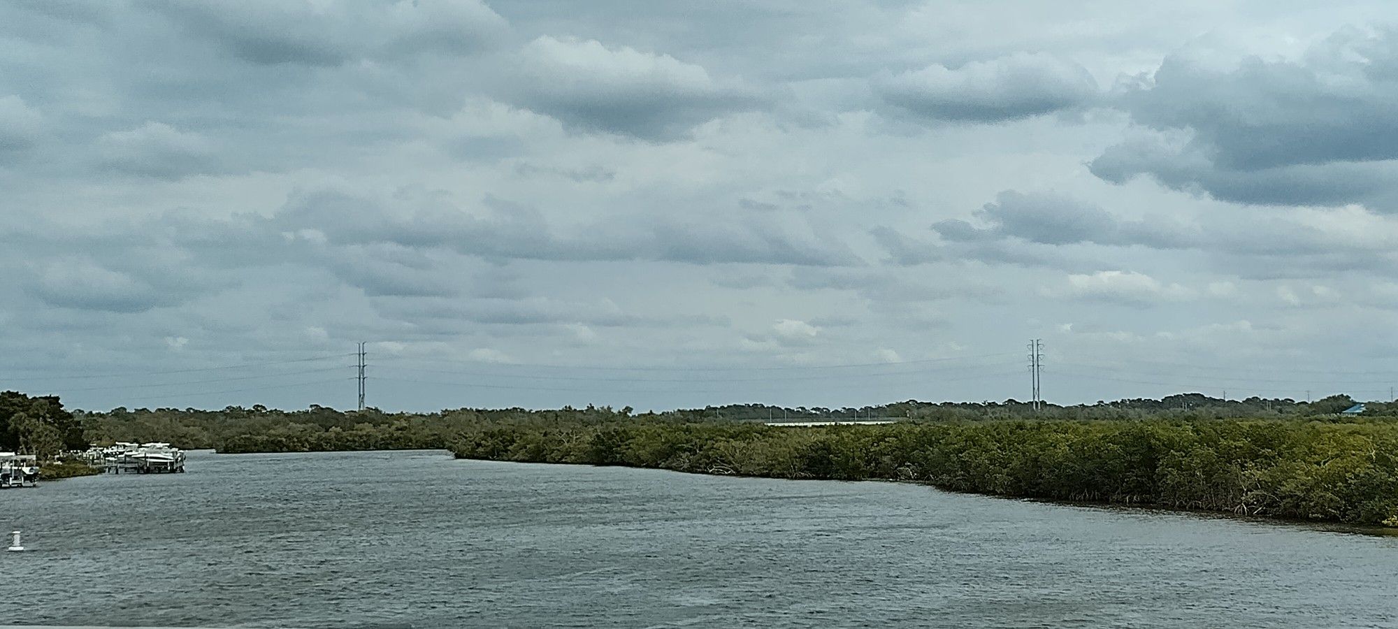 Wide river under a cloudy sky, flanked by lush green banks and distant towers. - Seven Springs loop