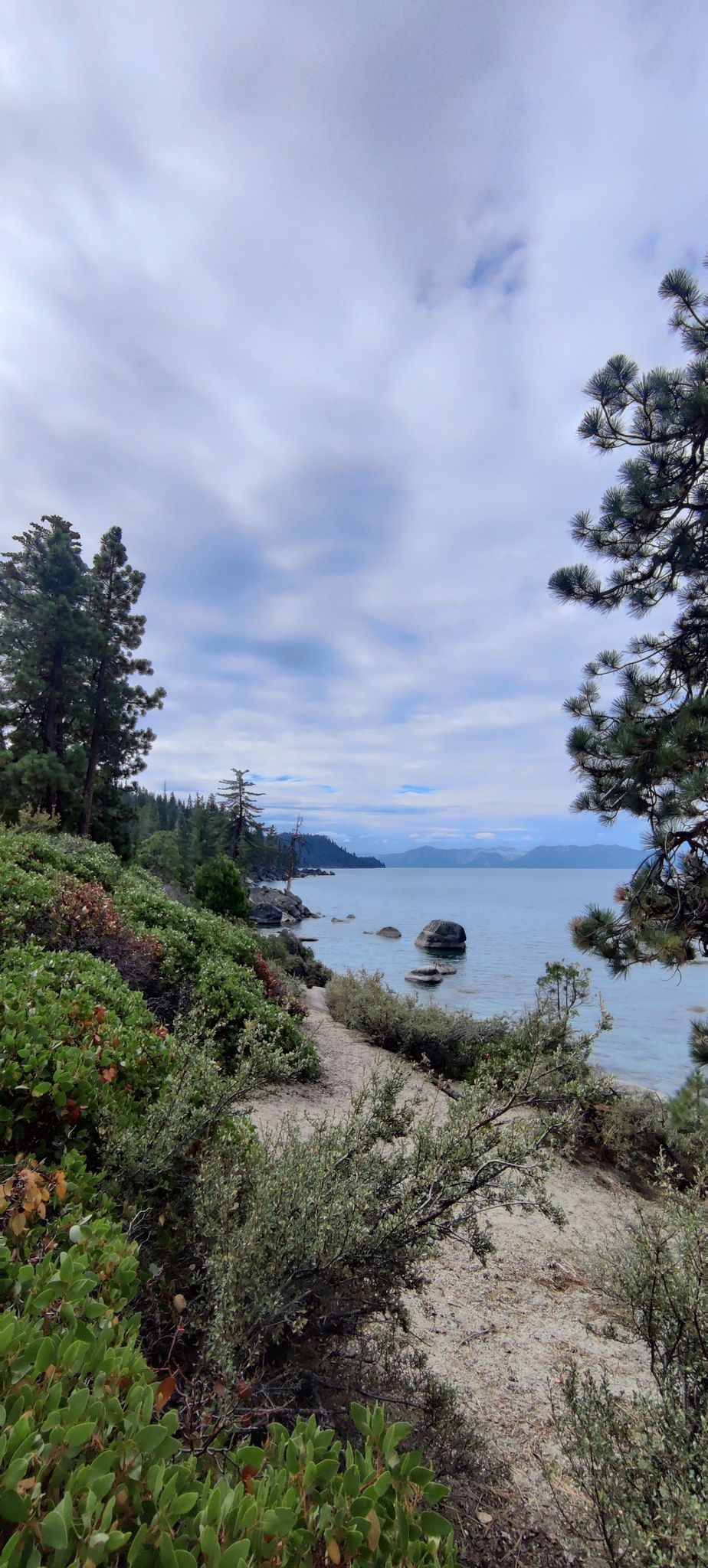 Overcast sky above a winding path along a rocky, tree-lined lake shore. - Chimney Beach and Secret Cove Trail