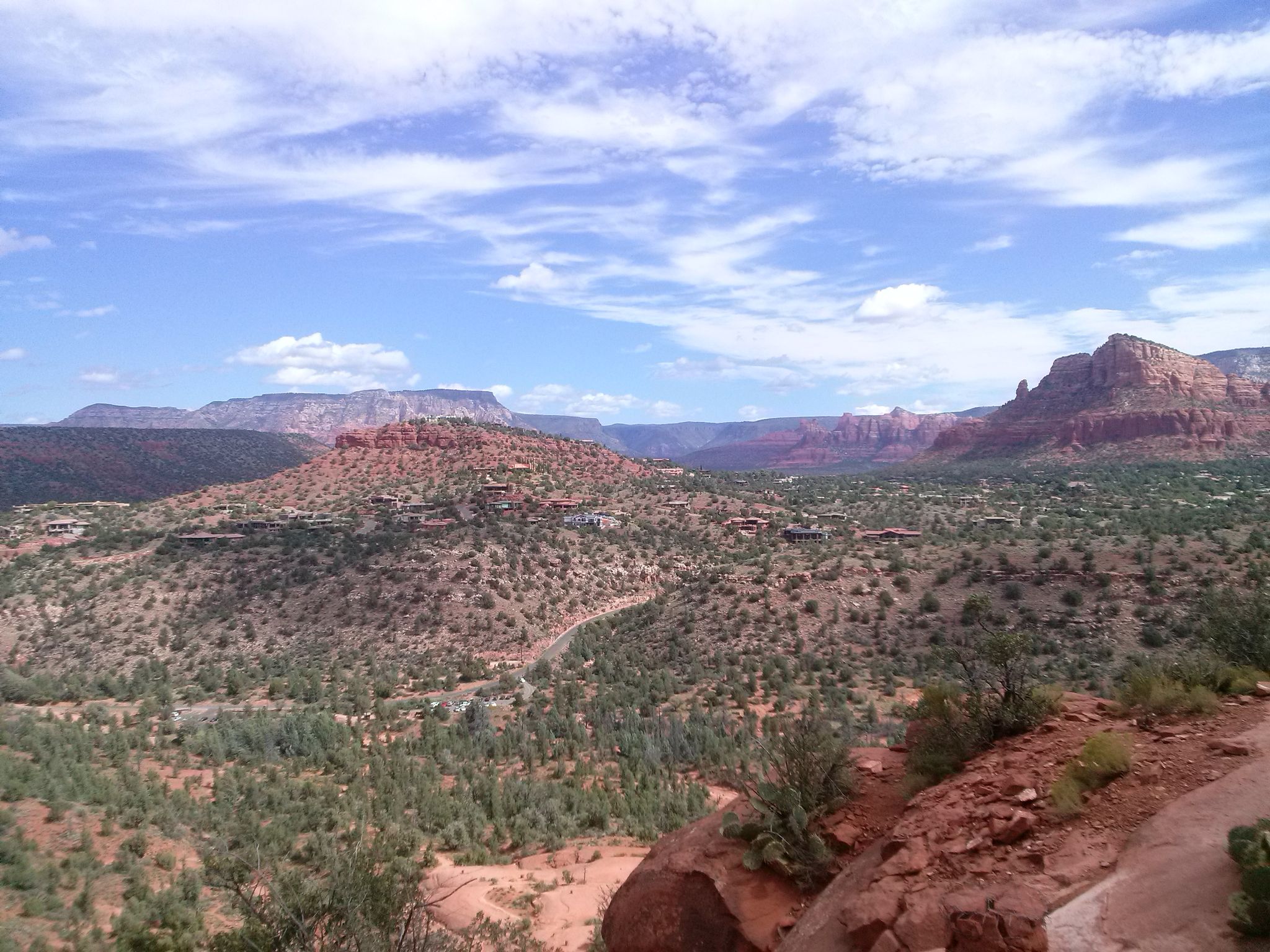 Wide desert landscape with red rock formations, green shrubs, and blue sky. - Cathedral Rock Trail