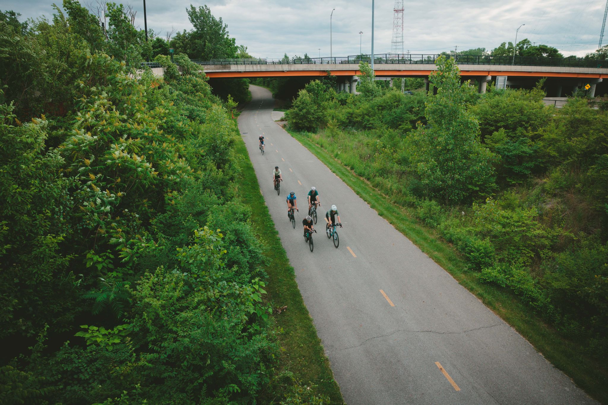 Group of cyclists riding on a paved path under a bridge, surrounded by trees. - Olentangy Trail loop from Grandview Heights
