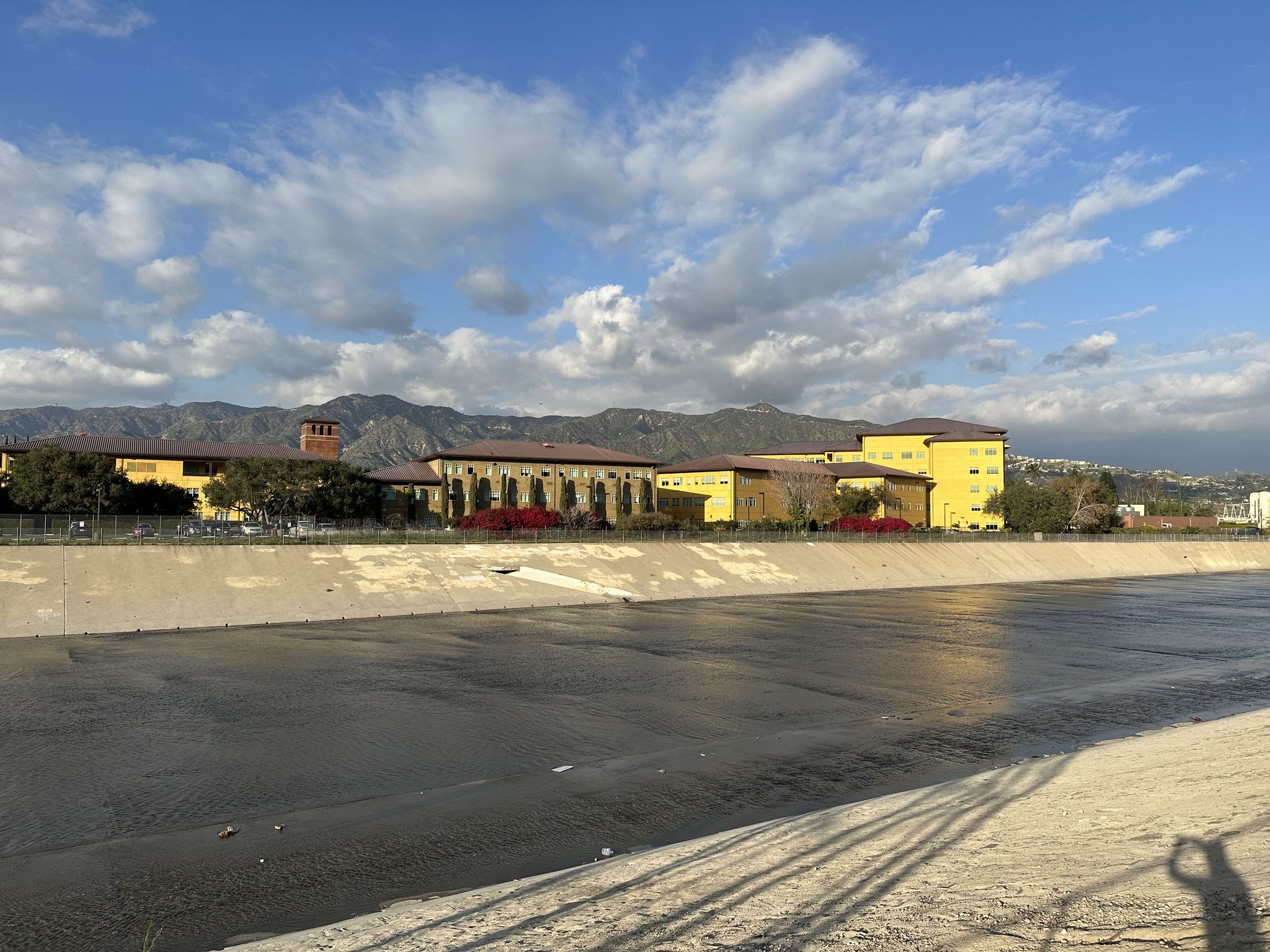 Concrete river channel with buildings and mountains under a partly cloudy sky. - Railway yard with steam trains – Toyon Trail loop from DreamWorks Studios
