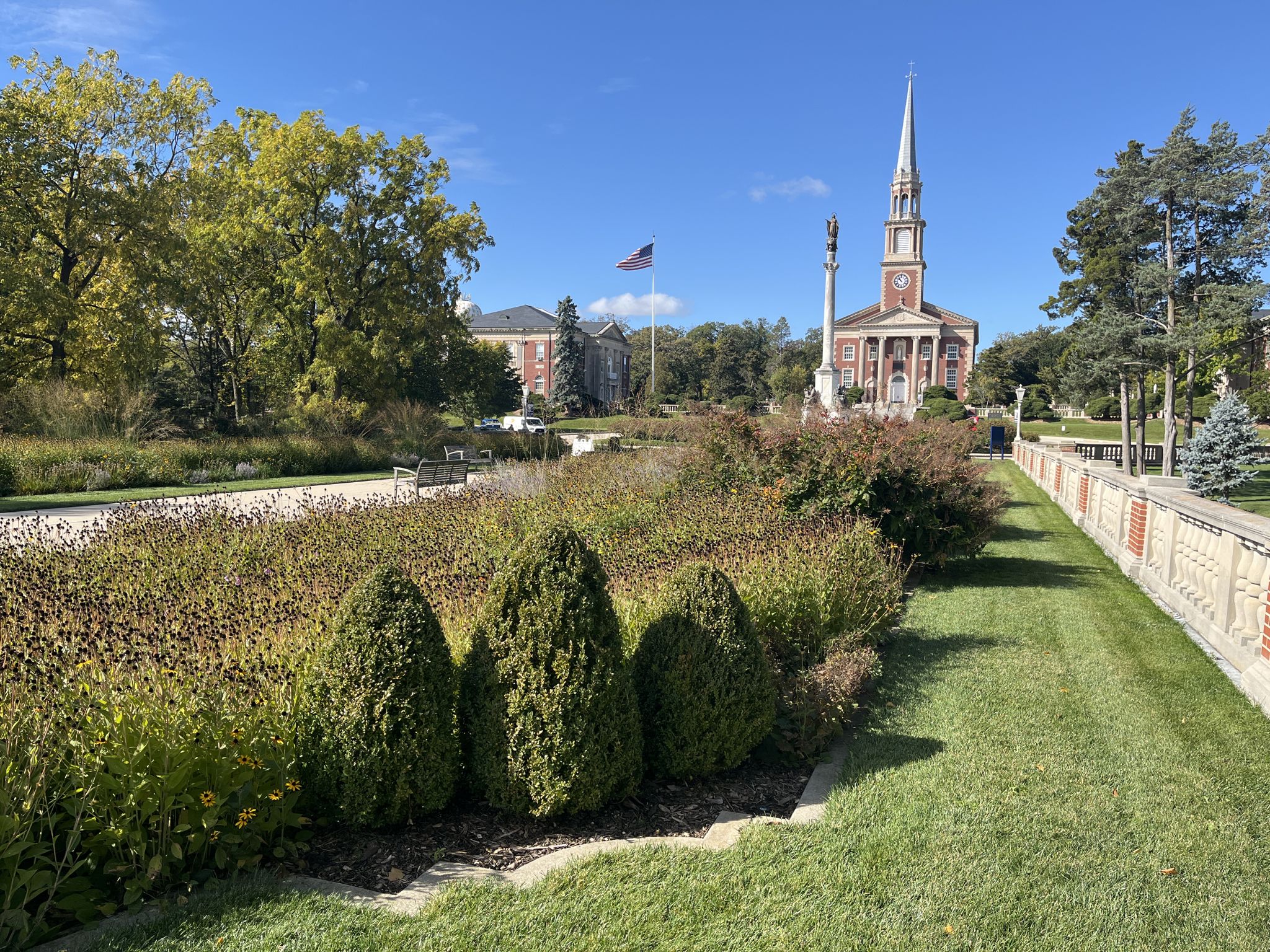 Church with a tall steeple overlooking a manicured garden on a sunny day. - Saint Mary's Lake loop via Lakeshore Drive