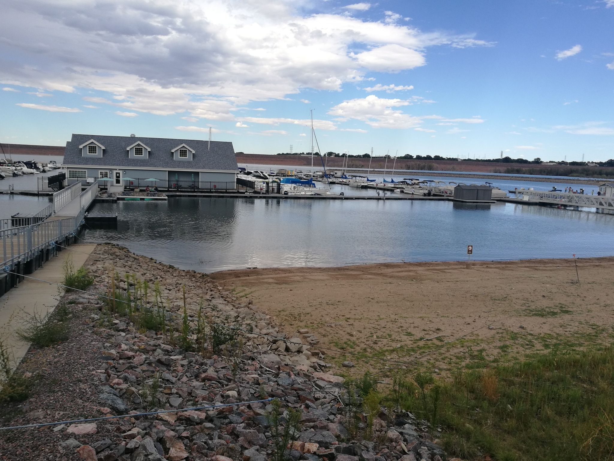 A marina with a building, many boats docked, and a sandy shore. - Chatfield Internal Trail
