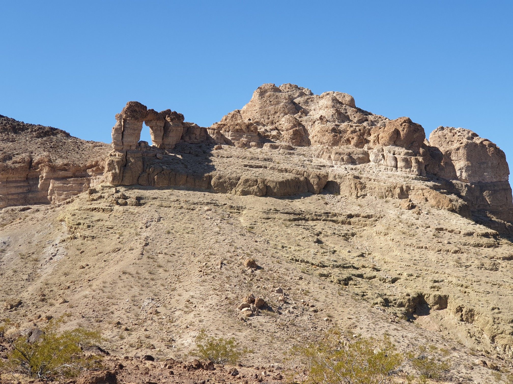 A natural rock arch formation on a dry, rocky mountain under a clear sky. - Liberty Bell Arch Trail
