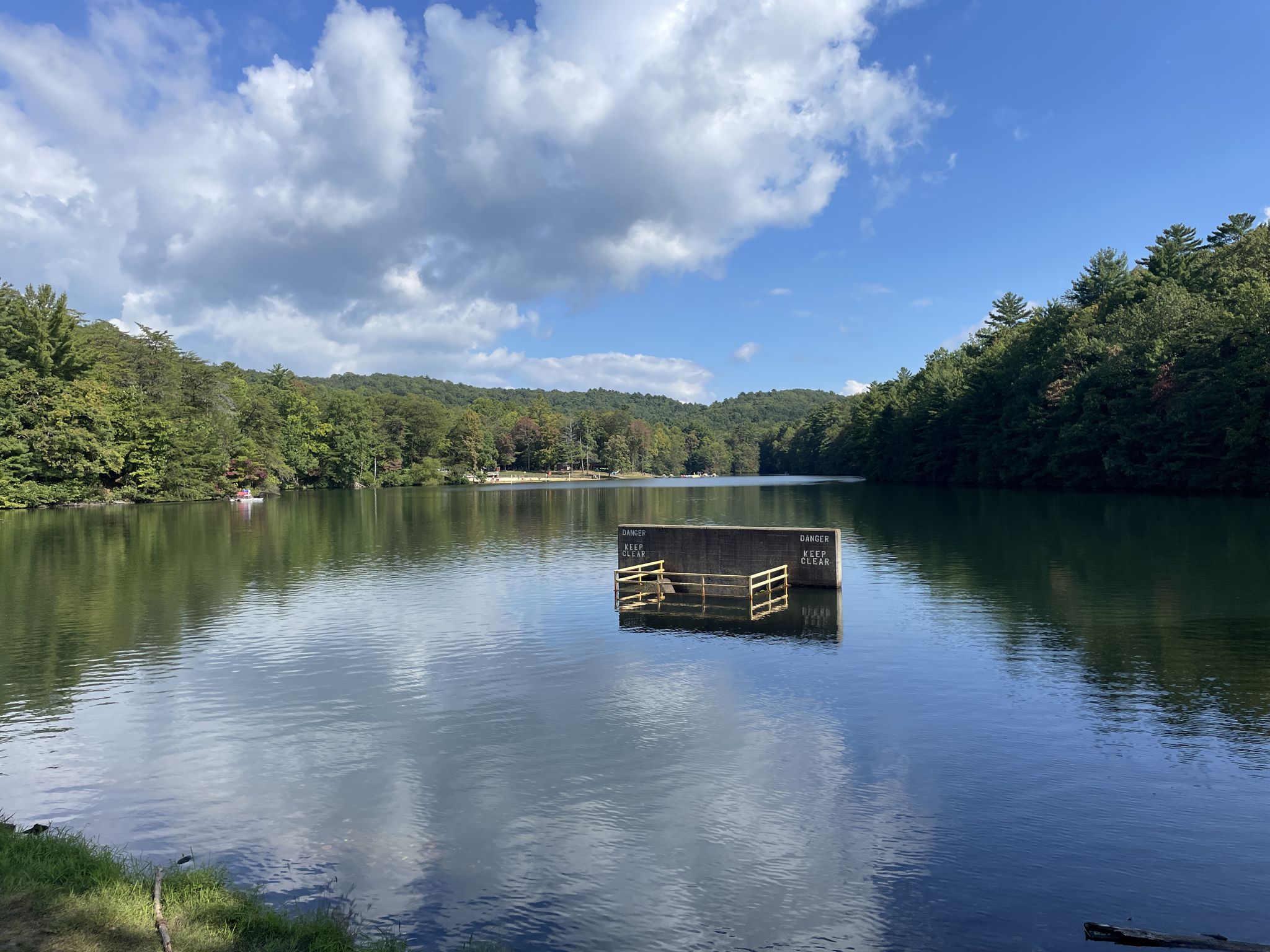 A calm lake surrounded by green forested hills under a bright, cloudy sky. - Fort Mountain Lake – Fort Mountain Lake loop from Fort Mountain State Park