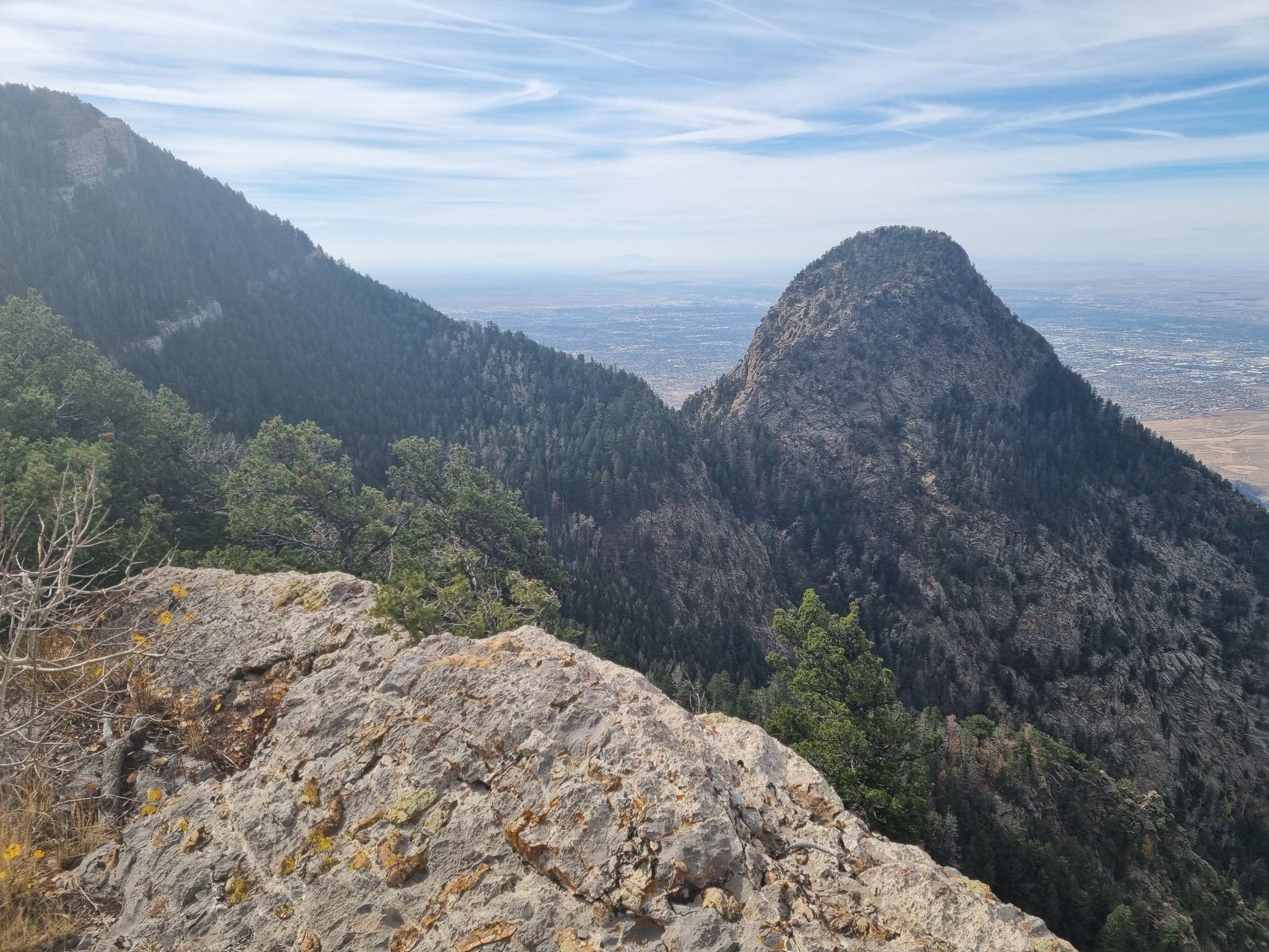 Rocky foreground overlooks forested mountain peaks and a distant valley on a clear day. - North Crest Trail