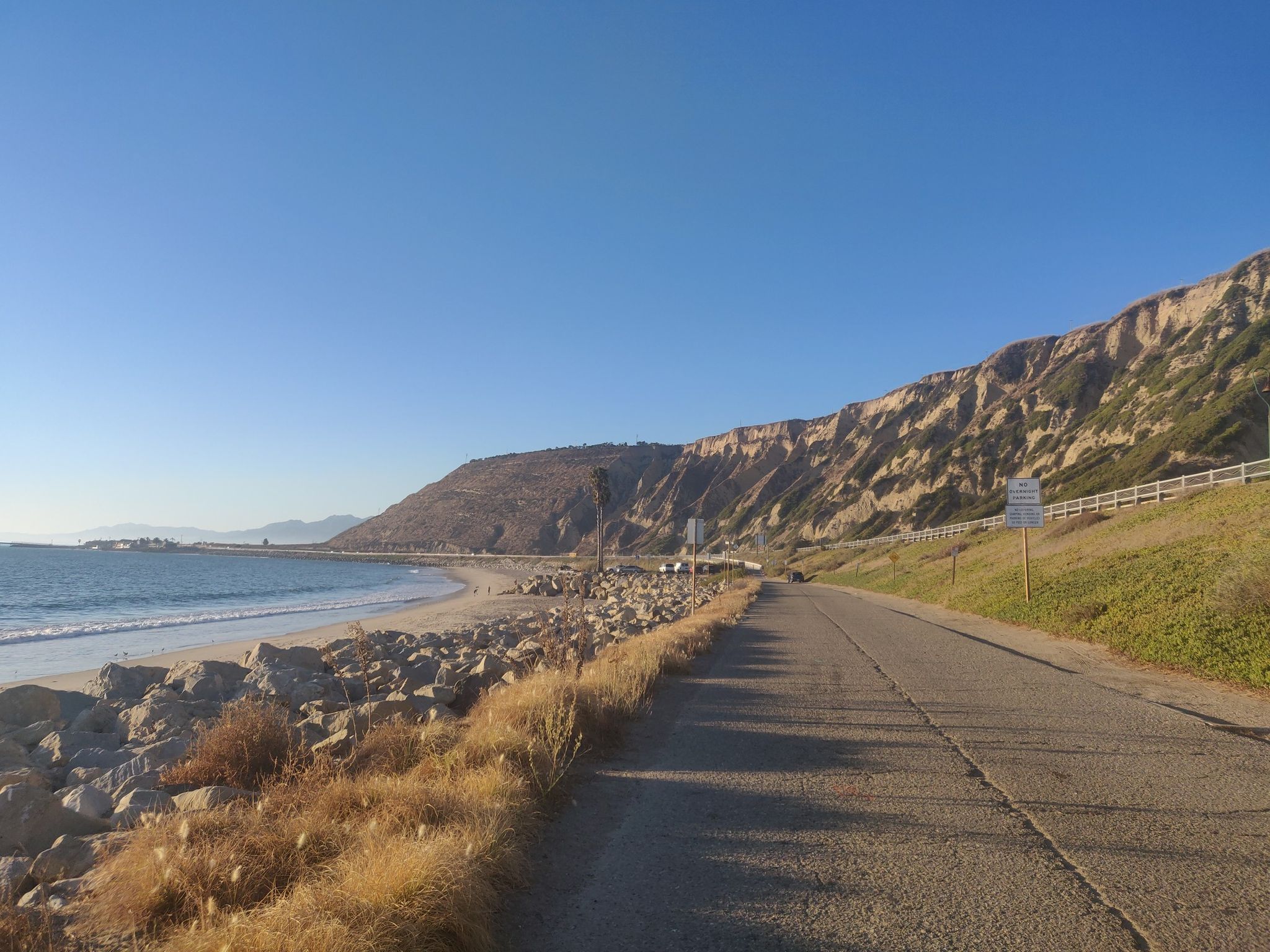 Coastal road beside a rocky beach and steep cliffs on a sunny day. - Lake Casitas loop