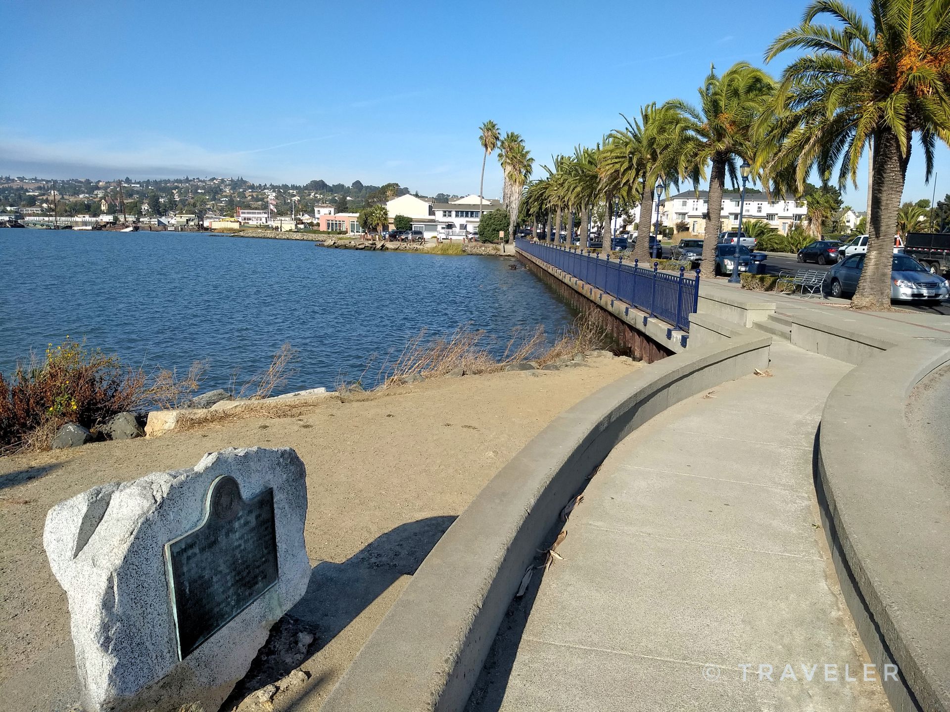 Sunny waterfront promenade lined with tall palm trees and a large stone marker. - Old State Capitol - Benicia – The Pony Express Memorial loop from Benicia