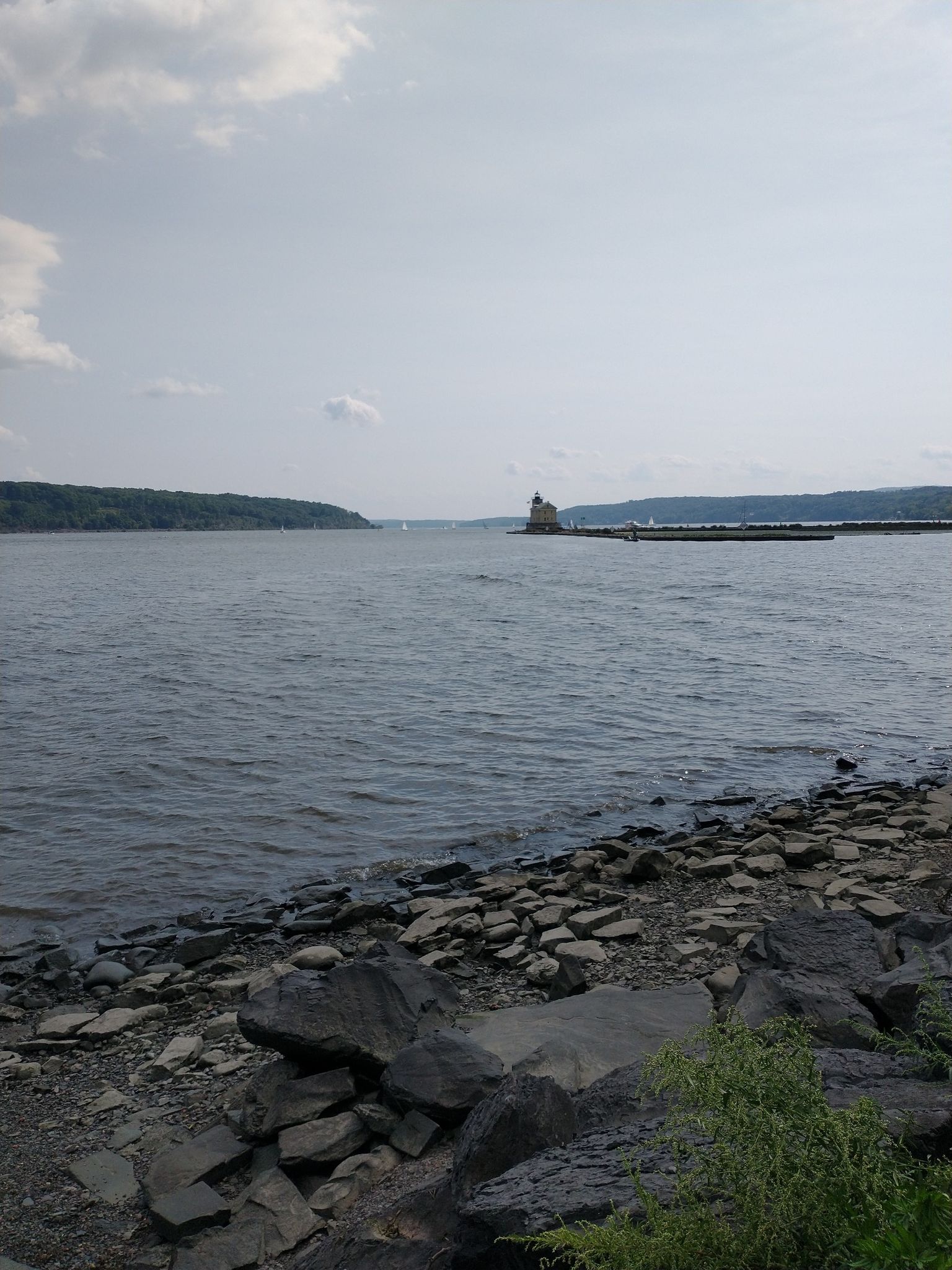 Rocky shore leading to wide water with a distant lighthouse and forested hills. - Rondout Creek loop from Kingston