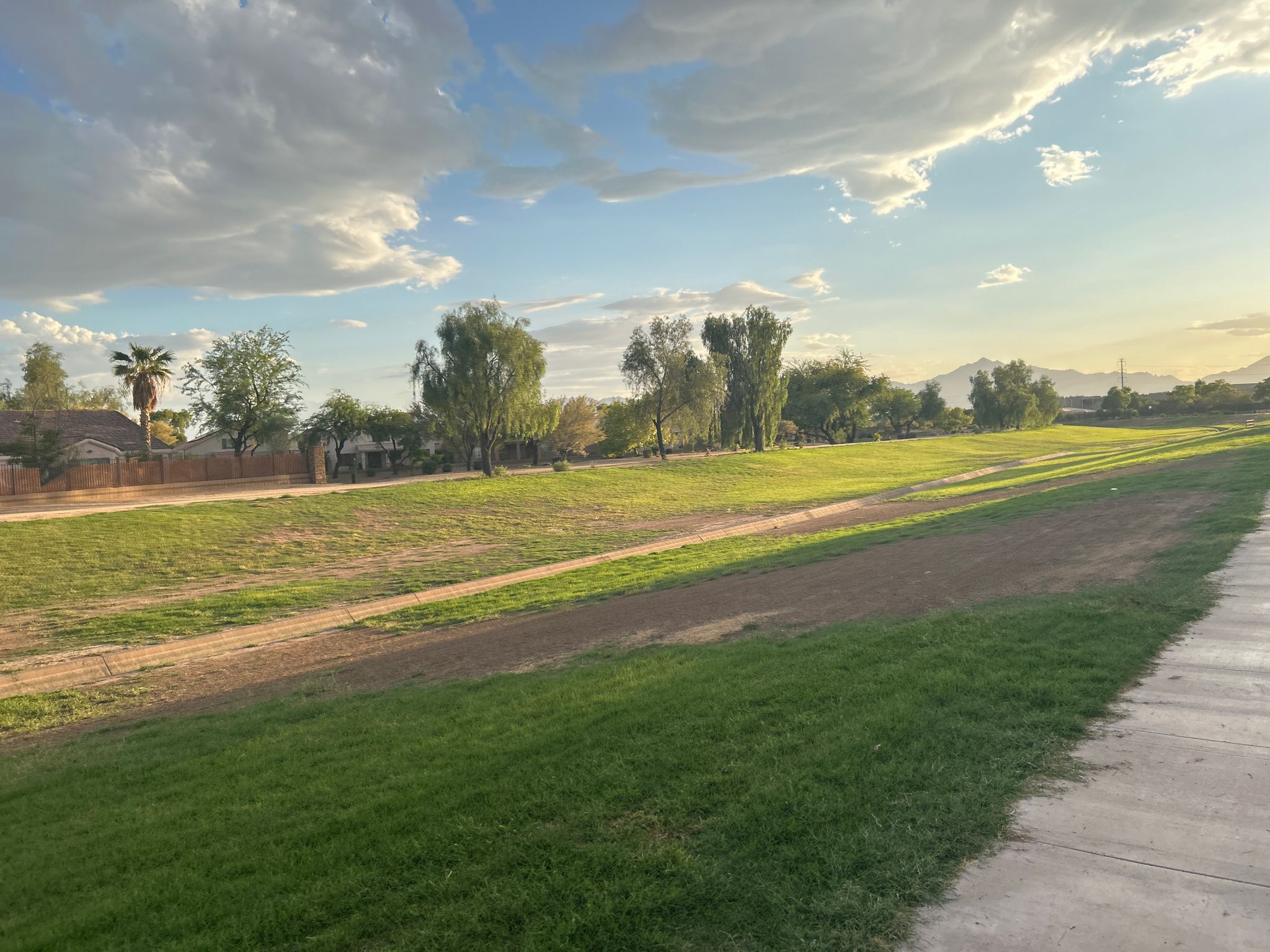 A wide grassy field with a sidewalk under a partly cloudy sky. - Laveen and Maricopa Trail Loop