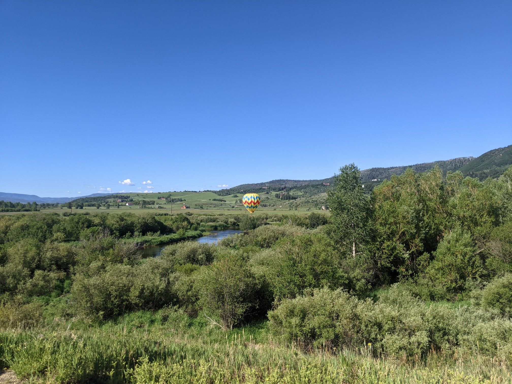 A colorful hot air balloon floats over a green valley with a river. - Casey's Pond loop from Resort Group