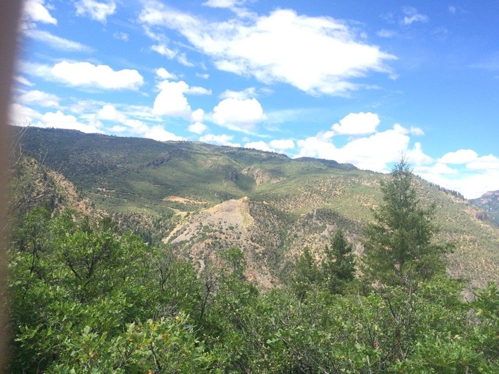 Expansive view of green, tree-covered mountains and a valley under a bright, cloudy sky. - View of Glenwood Springs – Glenwood Springs Scout Trail loop from Glenwood Springs