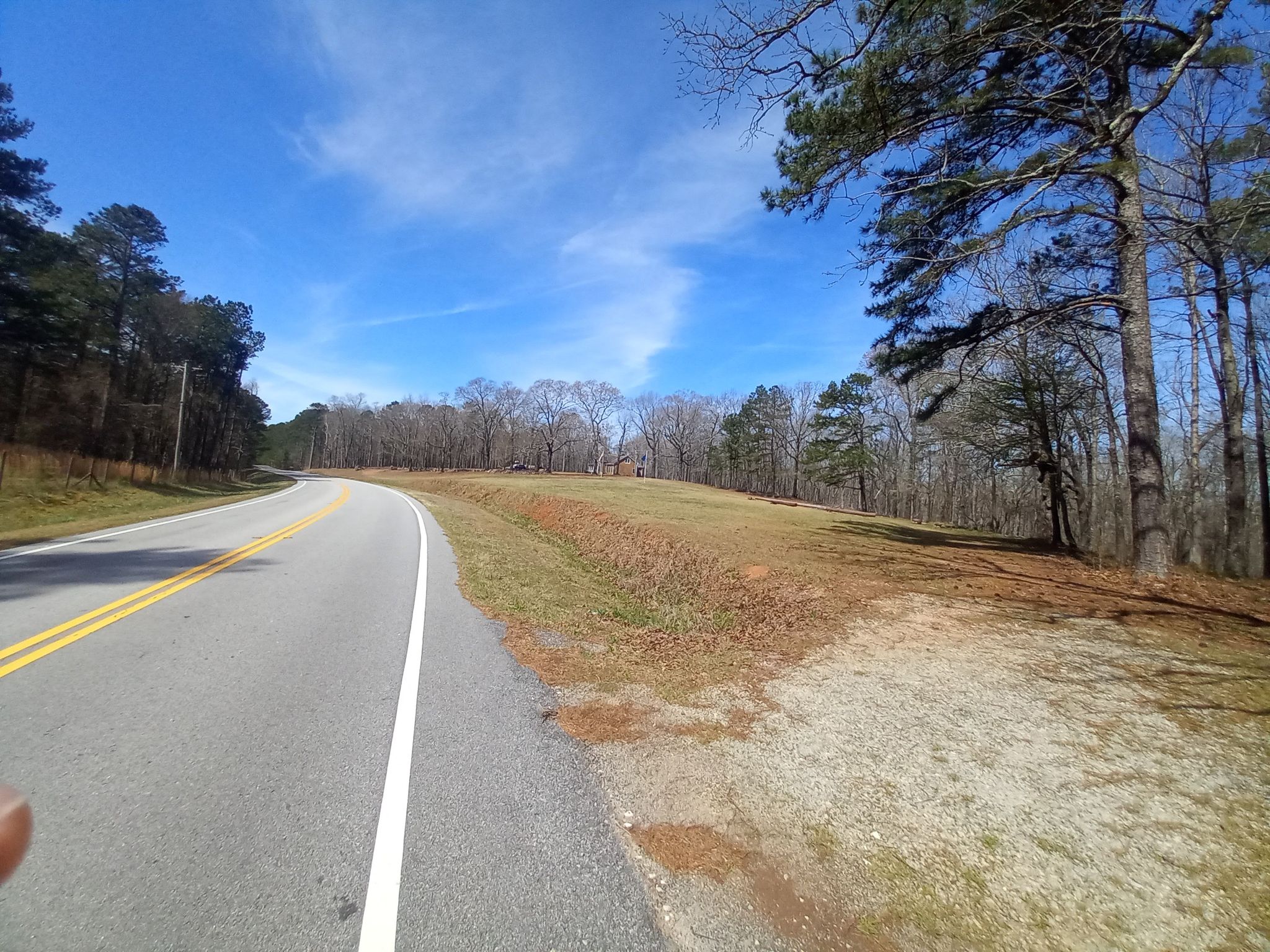A curved road next to a grassy field and forest under a bright blue sky. - Lake Peachtree Dam to Padgett Lake loop