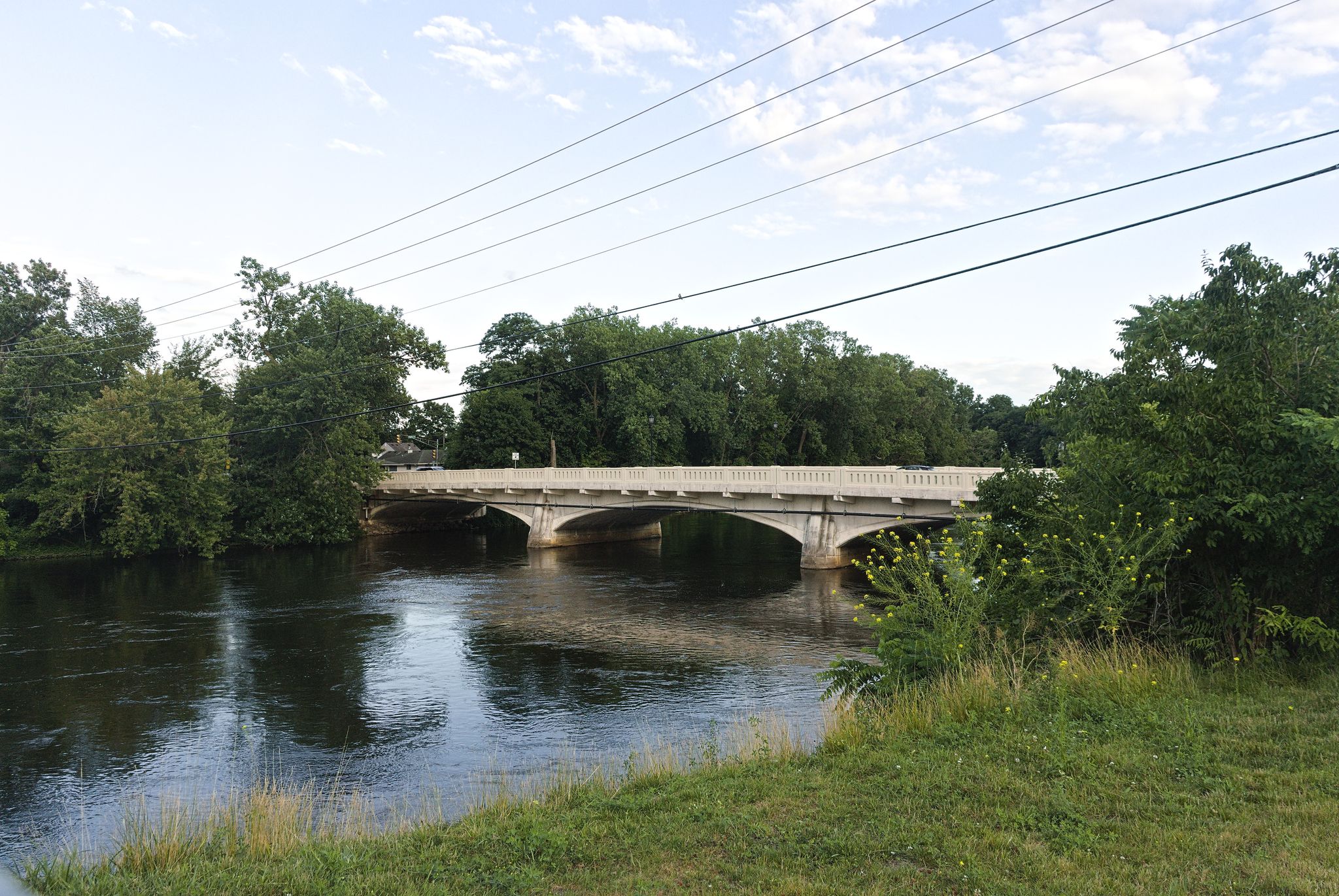 Concrete bridge over a river, surrounded by dense green trees under a bright sky. - Basilica of the Sacred Heart loop from South Bend