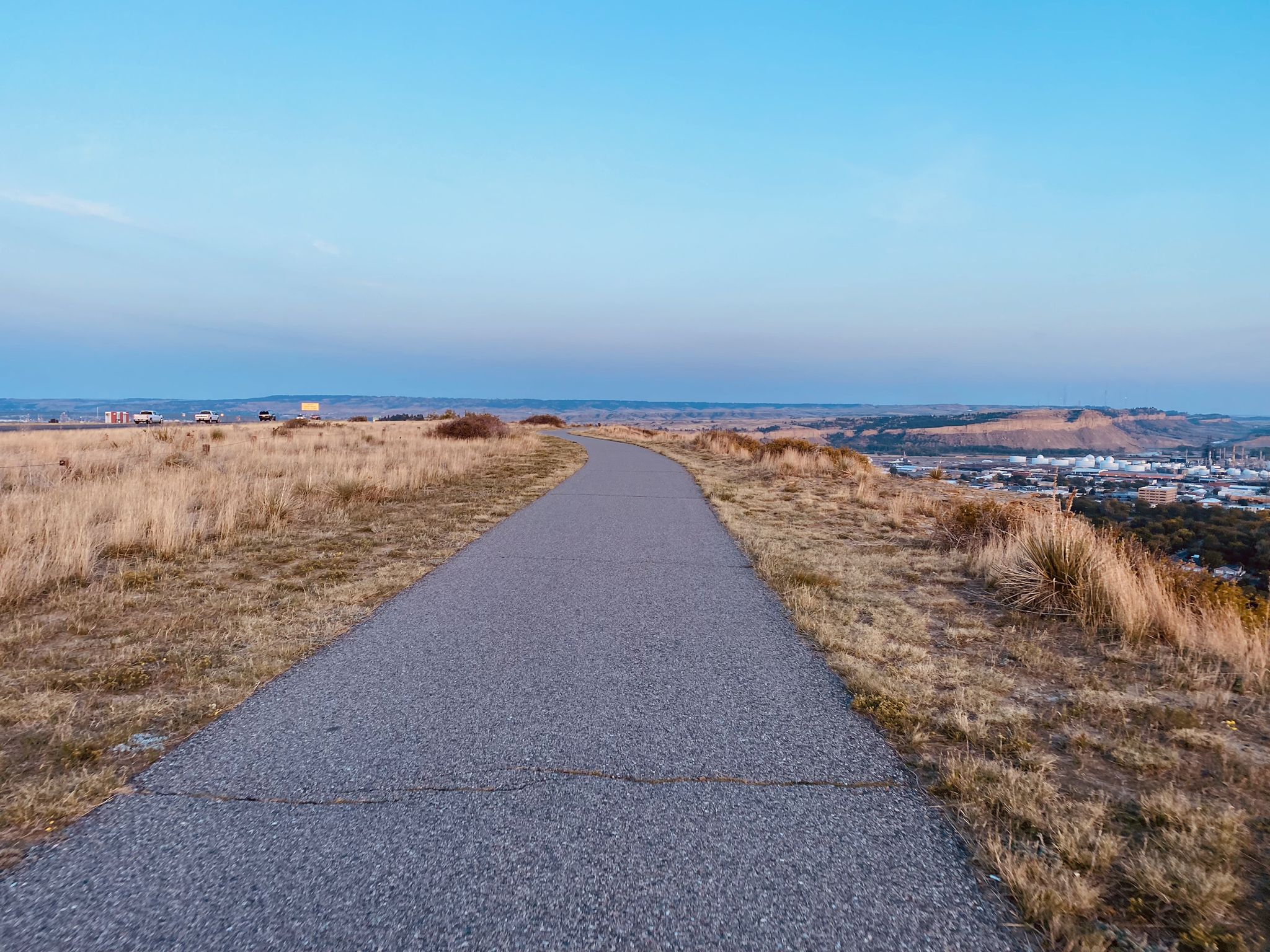 Paved path winding through dry grassy hills under a clear sky. - Chief Black Otter Trail