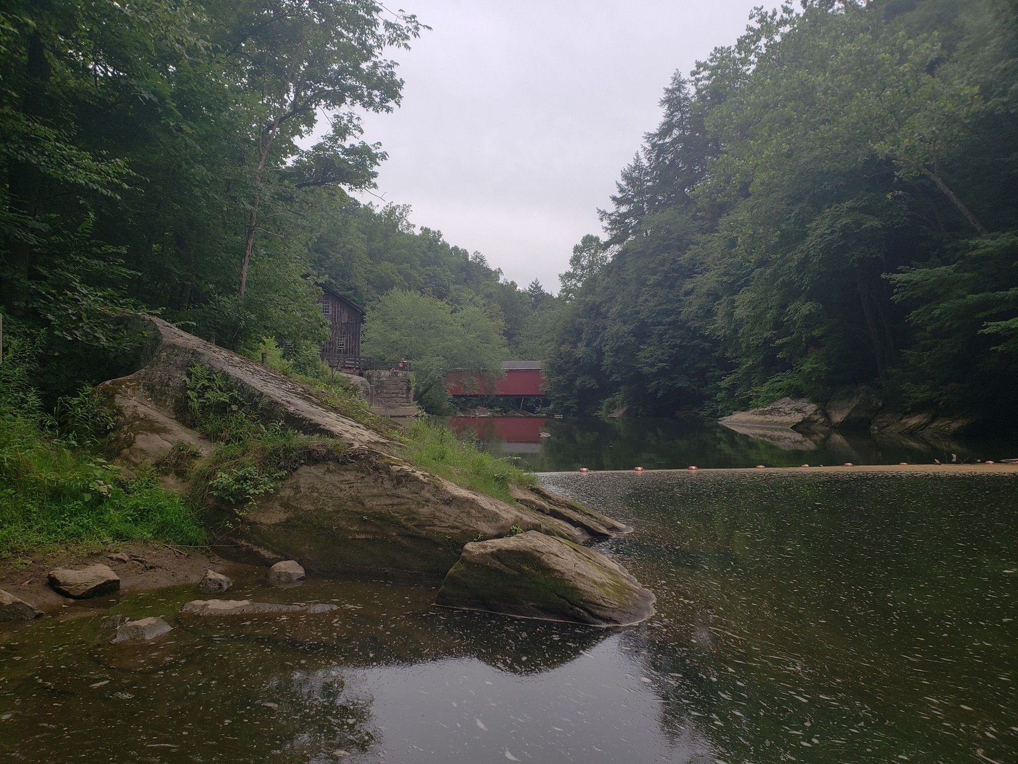 A calm river with large boulders, a distant red covered bridge, and forest. - Connoquenessing Creek – McConnells Mill State Park loop from Route 528 (Evans City) Park & Ride