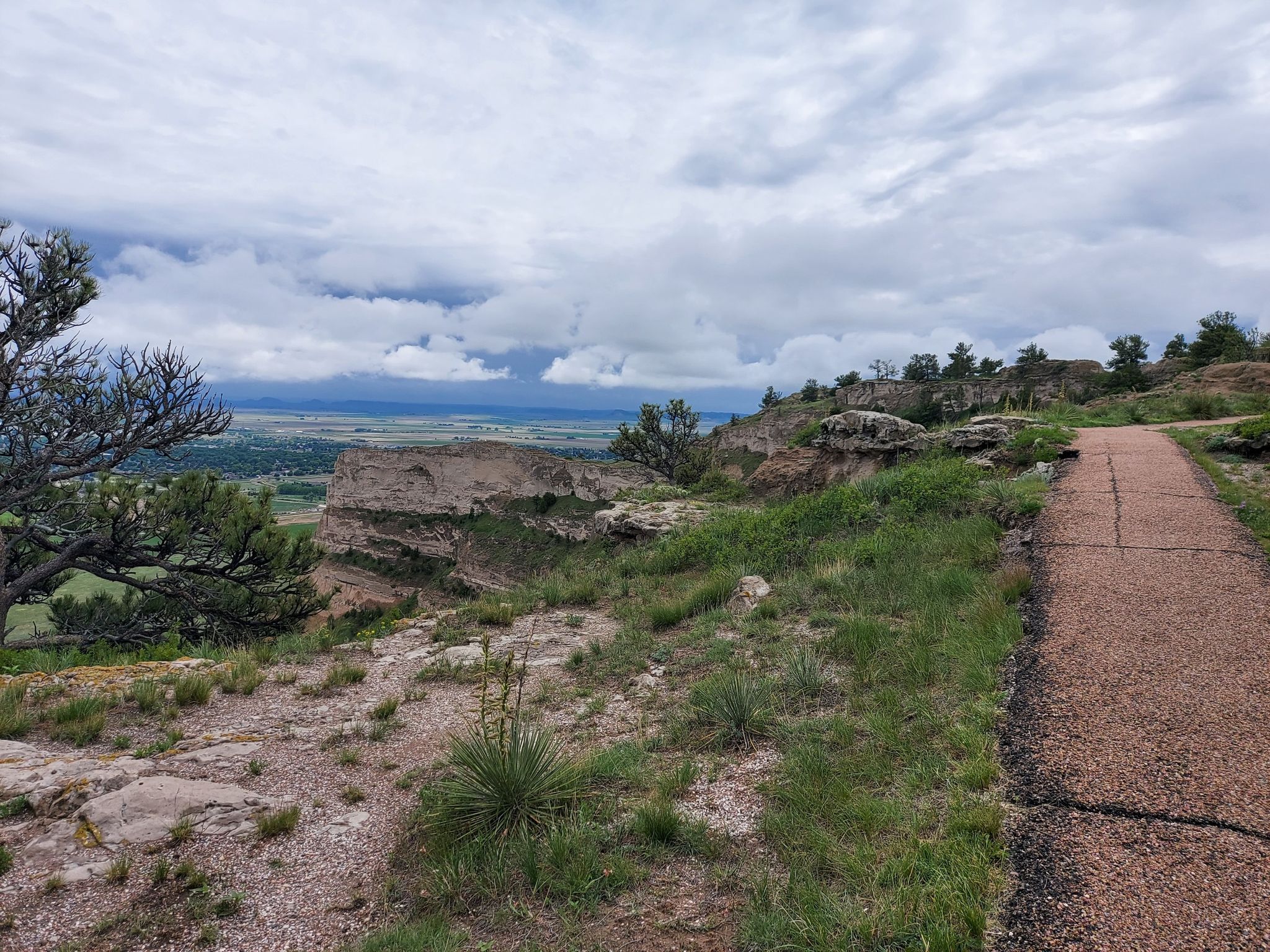 Paved path on a rocky hilltop with green grass and distant valley. - North Overlook Trail