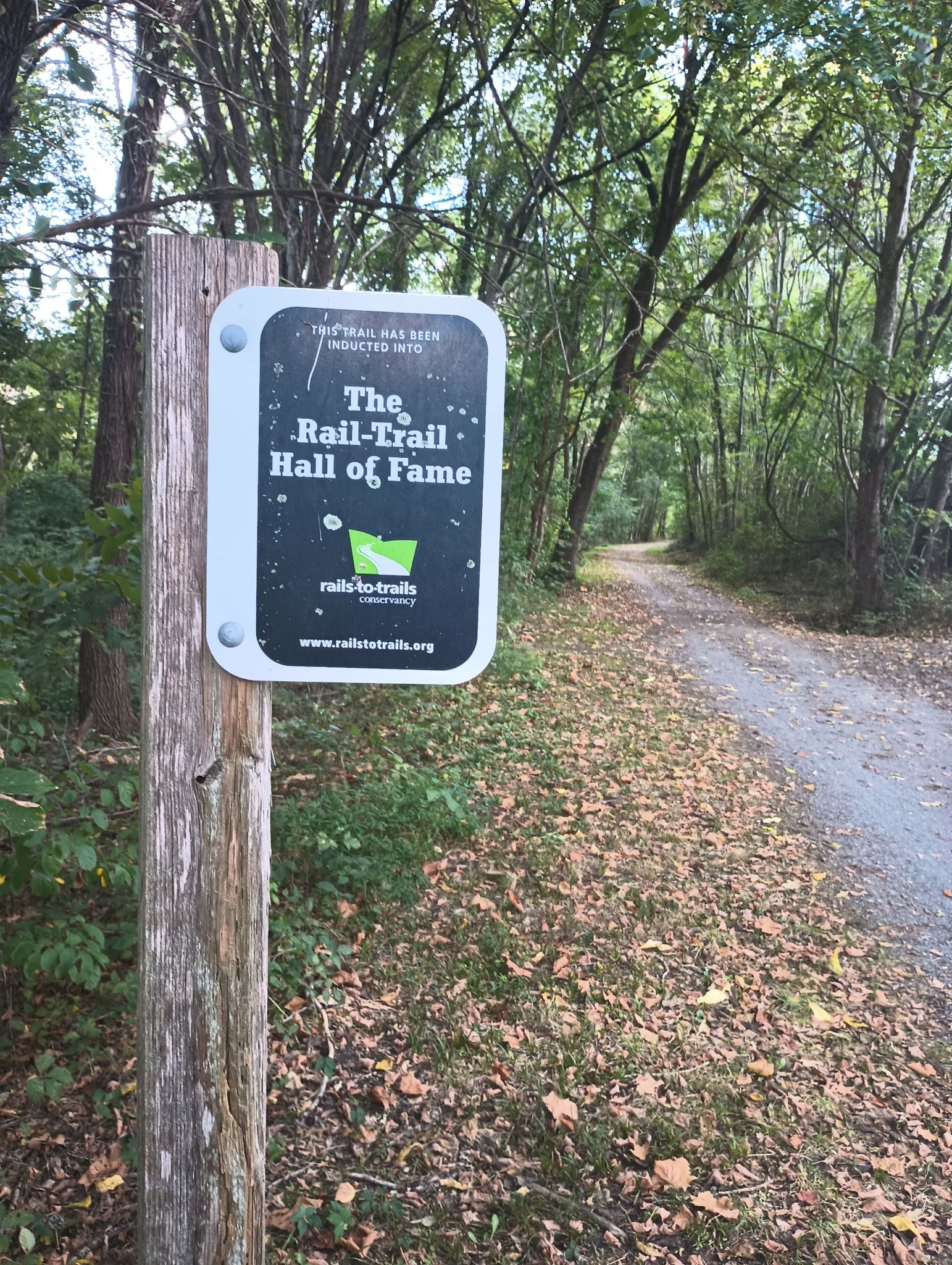A sign for 'The Rail-Trail Hall of Fame' stands beside a wooded path. - Damascus City Park loop from Garden