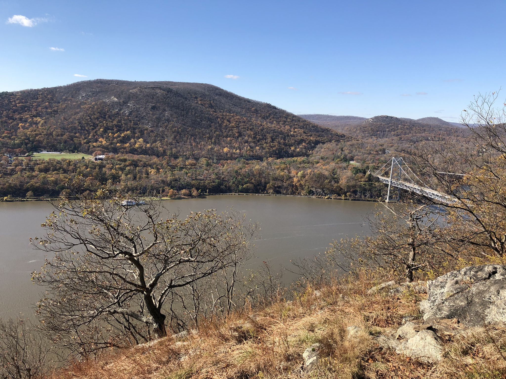 Sunny view of a river, forested hills, and a suspension bridge. - Anthony's Nose via Camp Smith Trail