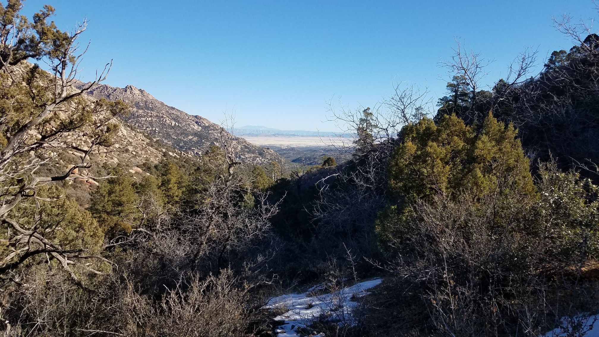 Forested mountain valley with patches of snow and a distant hazy plain. - Little Granite Mountain Loop