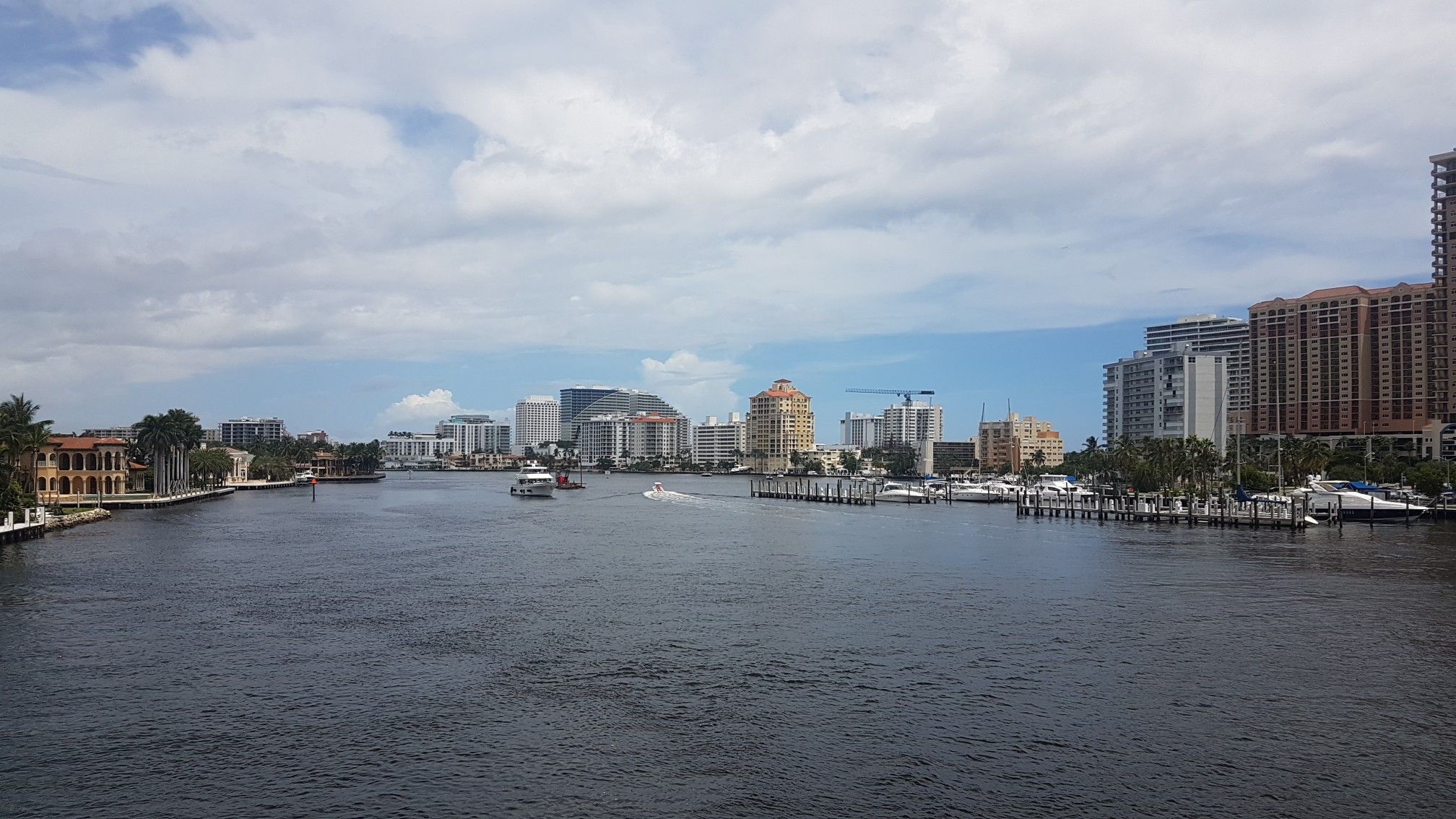 City skyline and boats on a wide river under a partly cloudy sky. - Las Olas and East Coast Greenway Loop