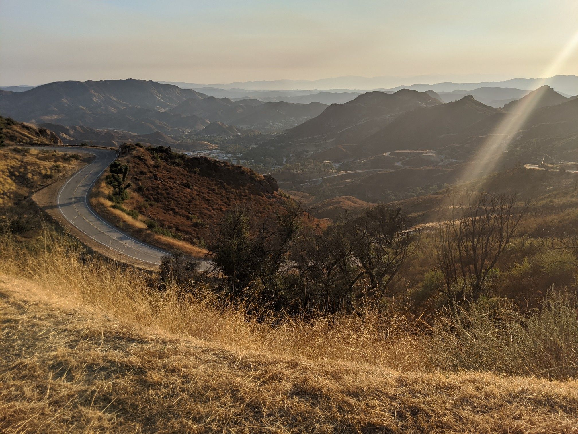 Winding road through dry hills at sunset, with golden sun rays. - Malibou Lake – La Sierra Preserve loop from Westlake Village