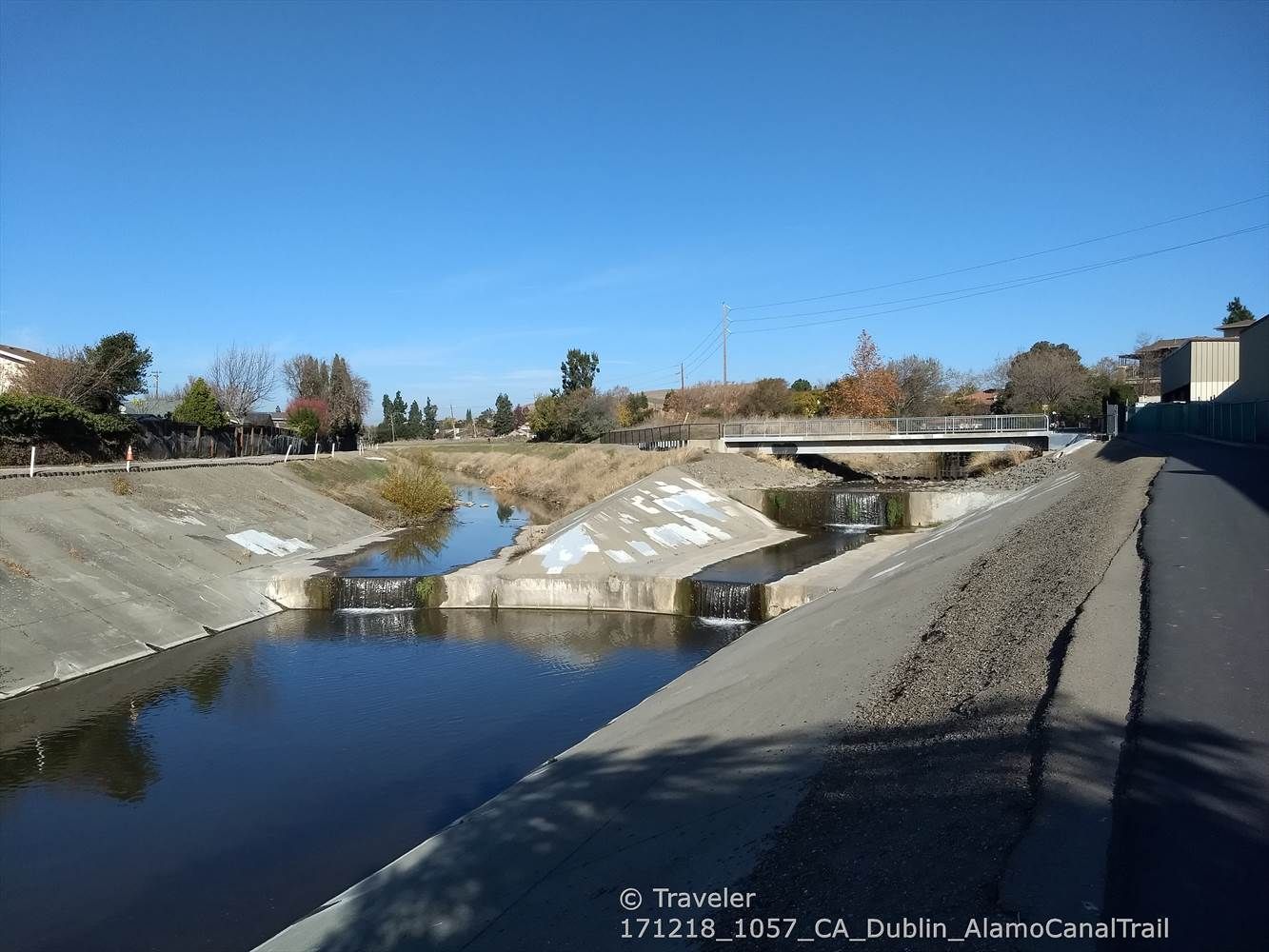 A concrete canal with water flowing over structures under a clear blue sky. - Running loop from Dublin