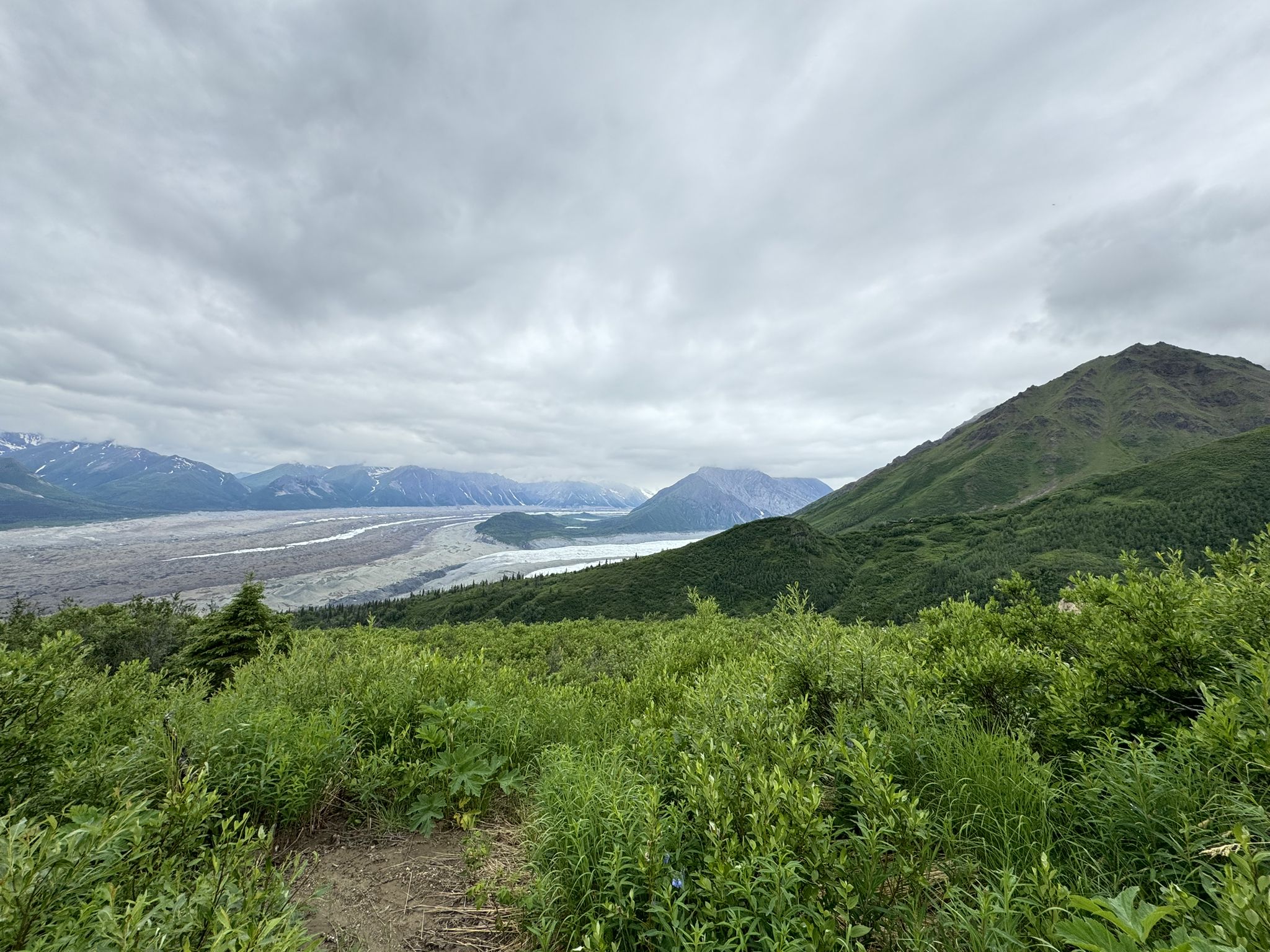 Overcast view of a wide river valley flanked by green and distant mountains. - Bonanza Mine Trail