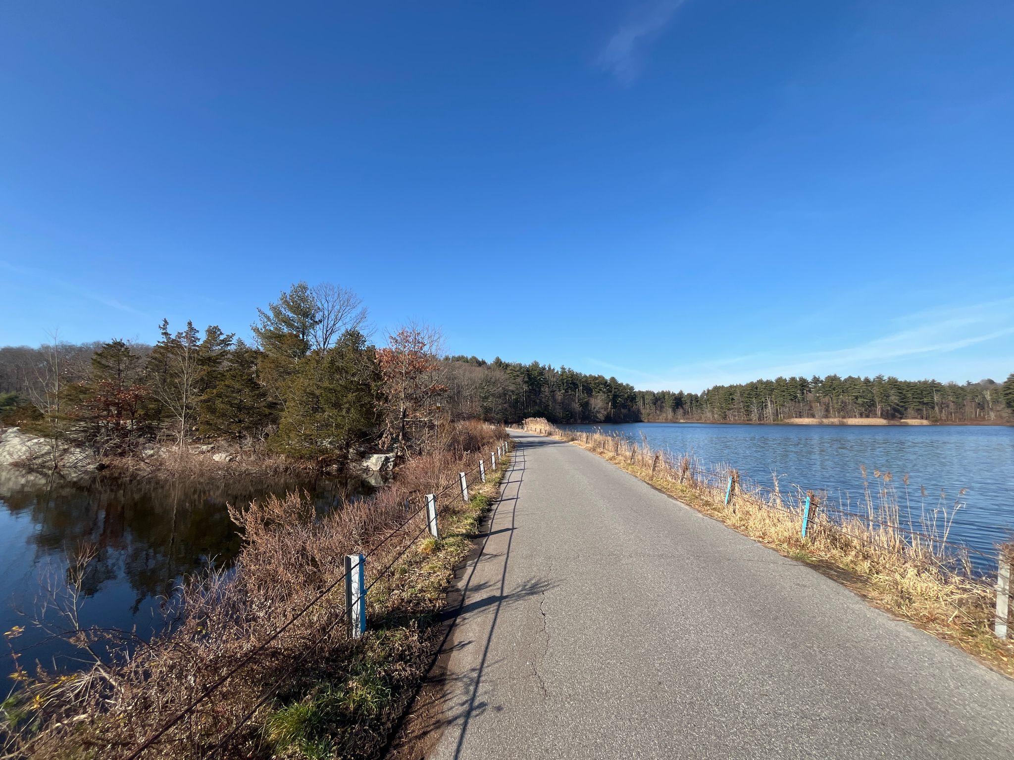 Paved road runs beside a calm lake under a clear blue sky. - Siscowit & South Norwalk Reservoir loop