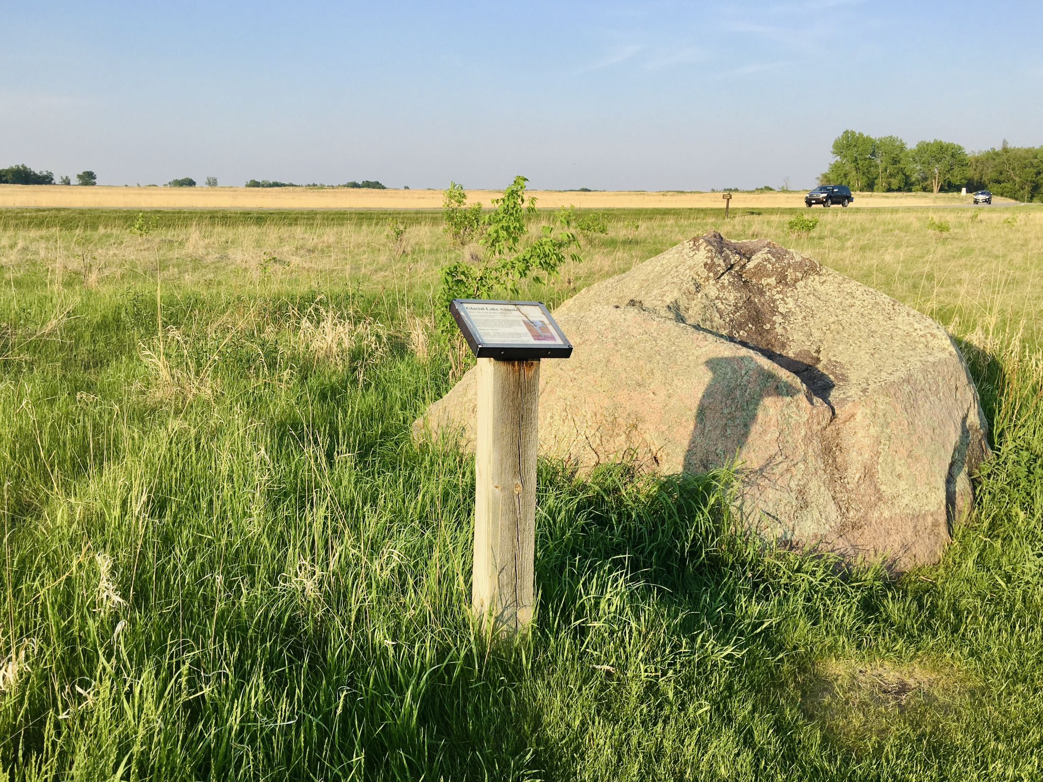 Wooden sign and large boulder in a sunny, grassy field. - Old Grade to River View to Wide Sky Trail
