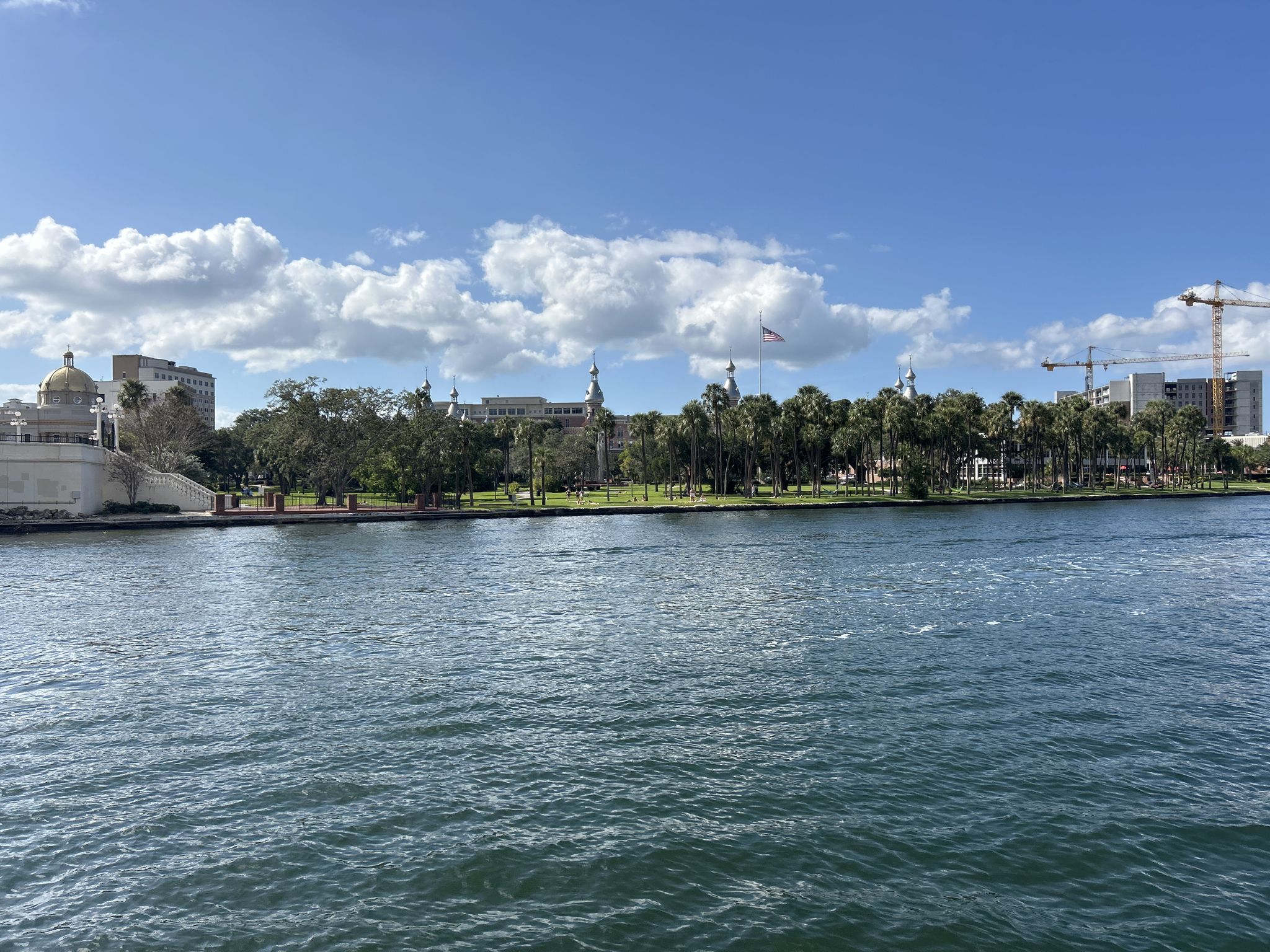 Riverfront view of ornate buildings and palm trees under a sunny sky. - Tampa Riverwalk