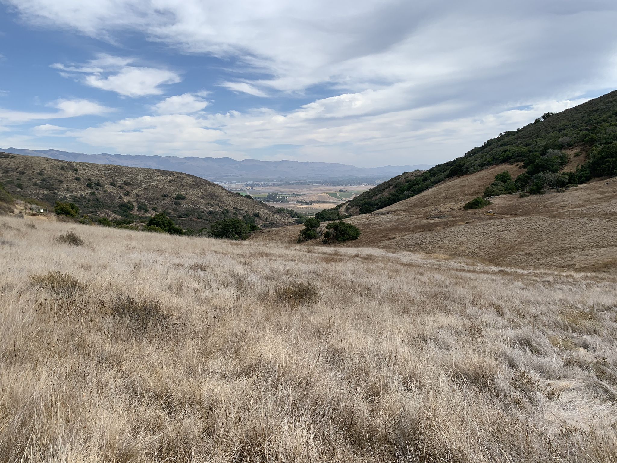 Expansive view of a valley between dry, grassy hills under a partly cloudy sky. - Edna Valley Vineyard – View of the SBP Airport loop from San Luis Obispo