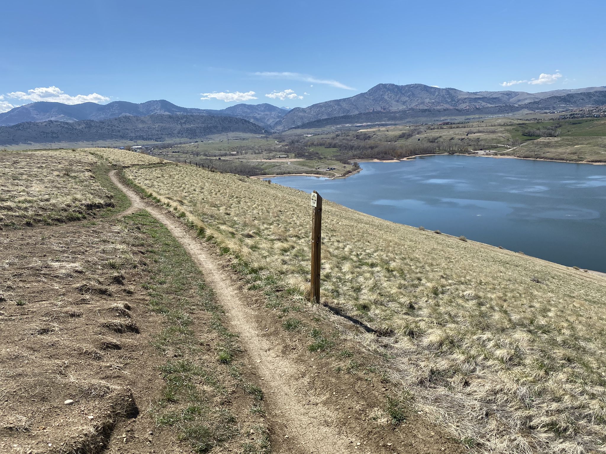 Dirt path on a grassy hill overlooking a blue lake and distant mountains. - Mount Carbon Loop
